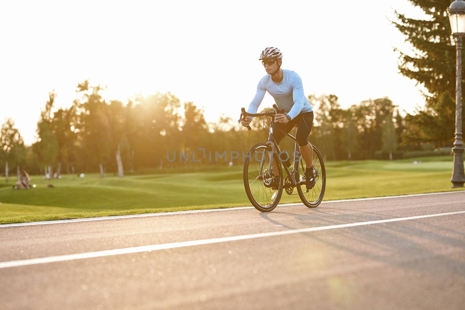 Perfect cycling season. Athletic man in sportswear, professional bicycle racer in sportswear riding mountain road bike in the city park at sunset by friendsstock