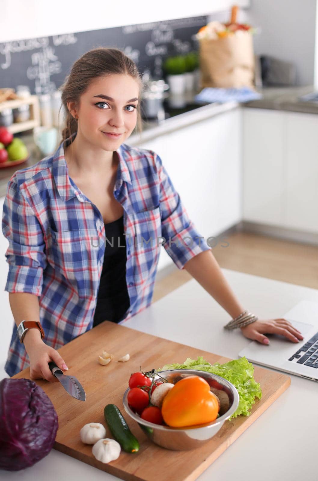 Young woman cutting vegetables in kitchen near desk. by lenetstan