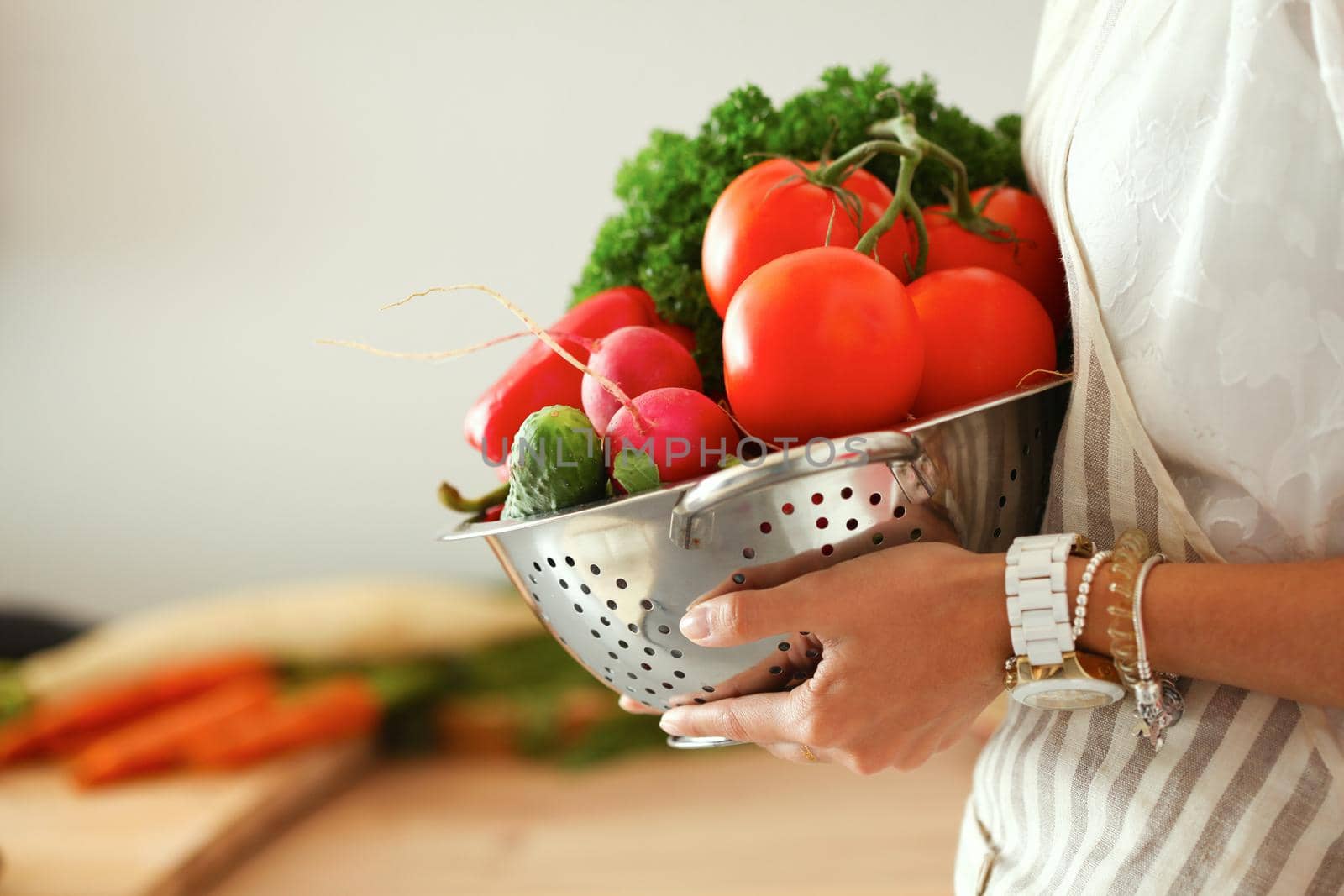 Young woman holding vegetables standing in kitchen .