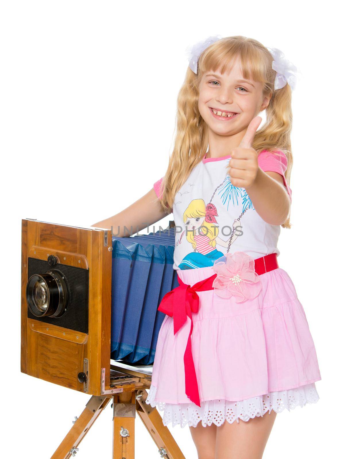 Laughing little girl with long blond ponytails on your head posing with an old camera. The girl held out her hands raised in the Upper thumb . Gesture all right . close-up