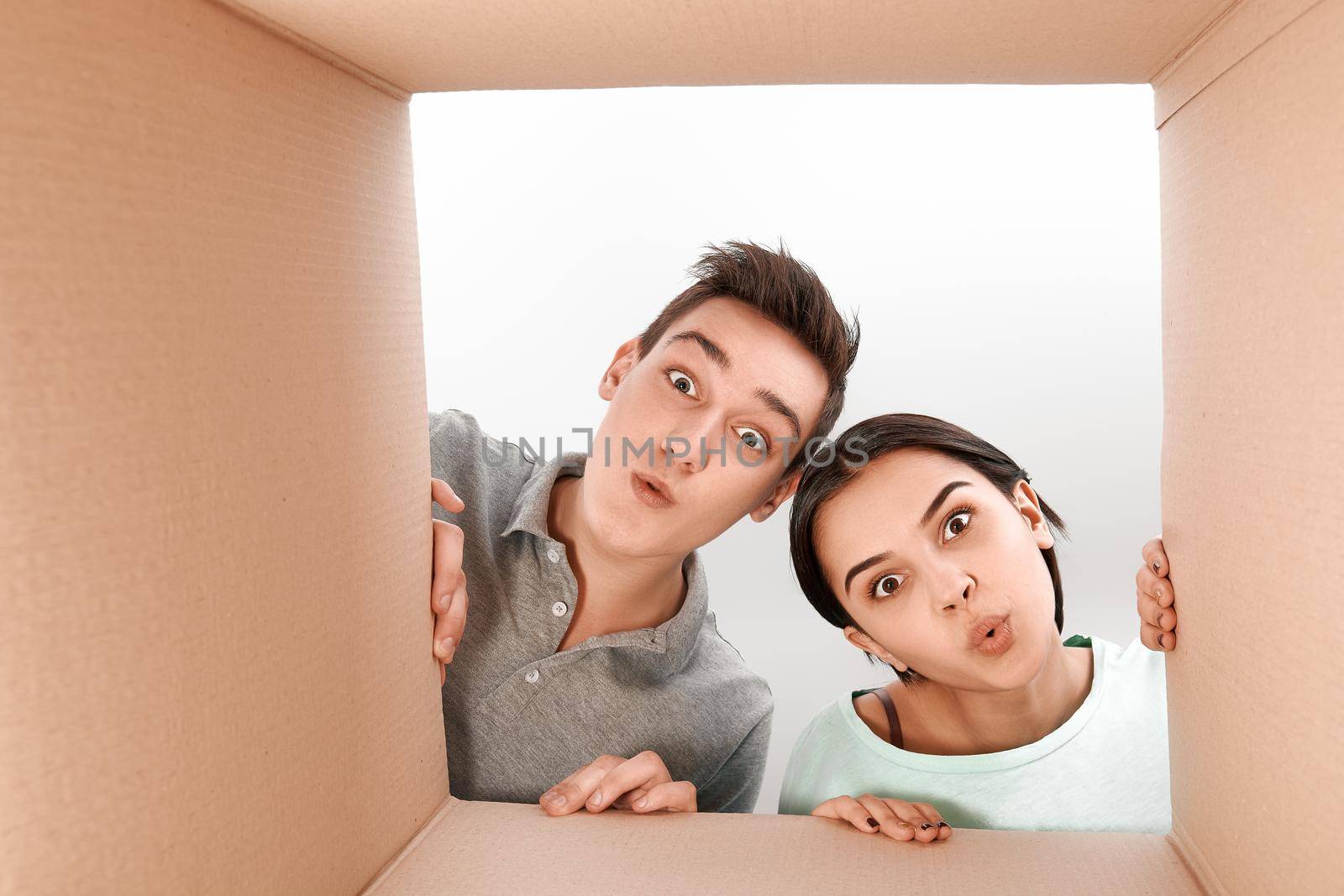 Cheerful teen couple unpacking, opening carton box and looking inside with a smile on their faces. They are delighted with the speed of delivery of goods. Human emotions and facial expressions concept