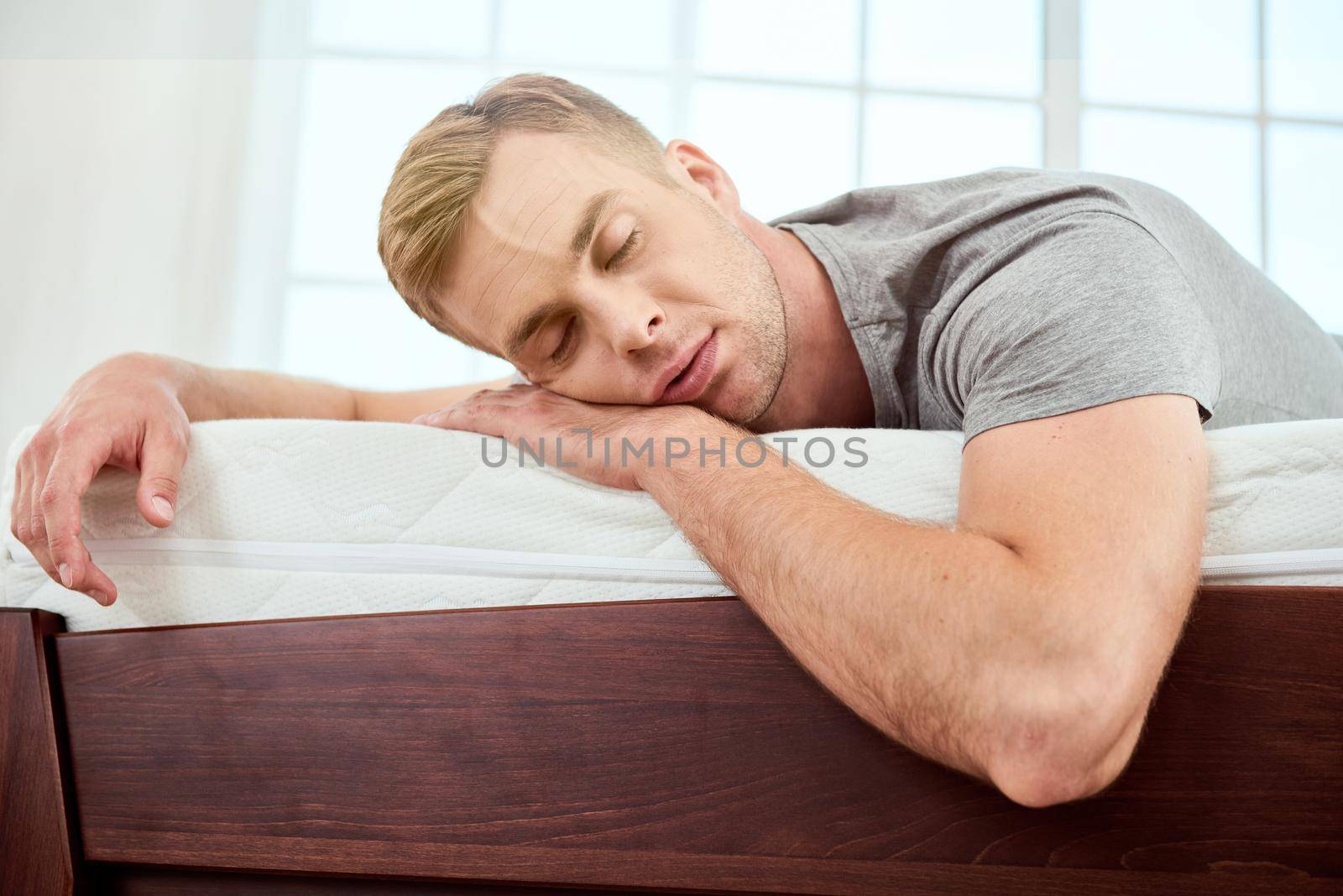 Young handsome man sleeping on a big and comfortable orthopedic white mattress in bedroom. Having a nap. Feeling tired. Home