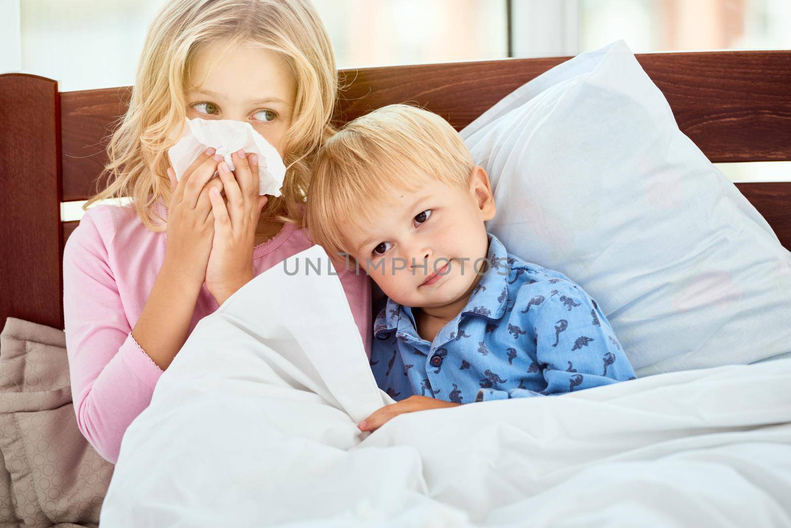 Little sister and brother with runny noses suffering from flu or cold while lying in bed together at home. Virus disease. Coronavirus concept. Sick family at home. Health concept