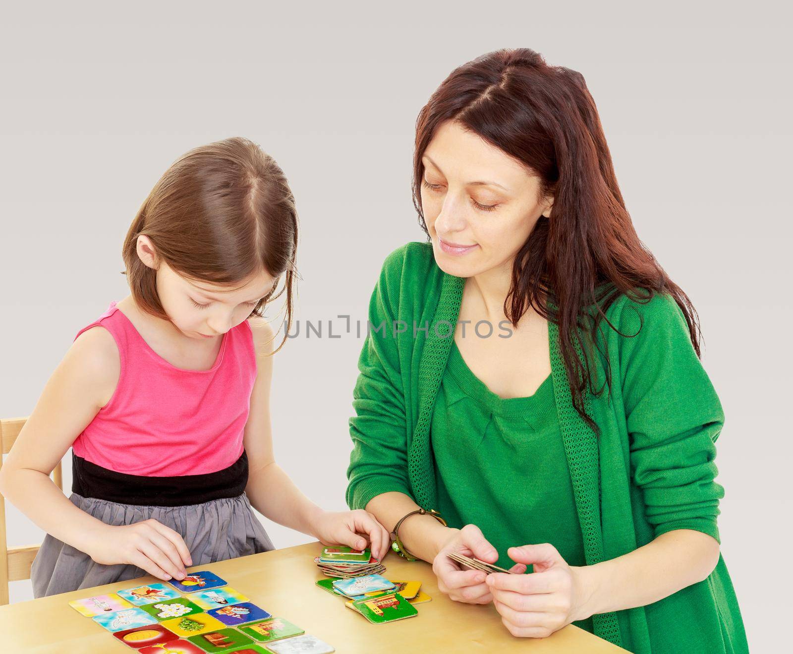 Cute little girl and her mother at the table laid out cards with pictures.On a gray background.
