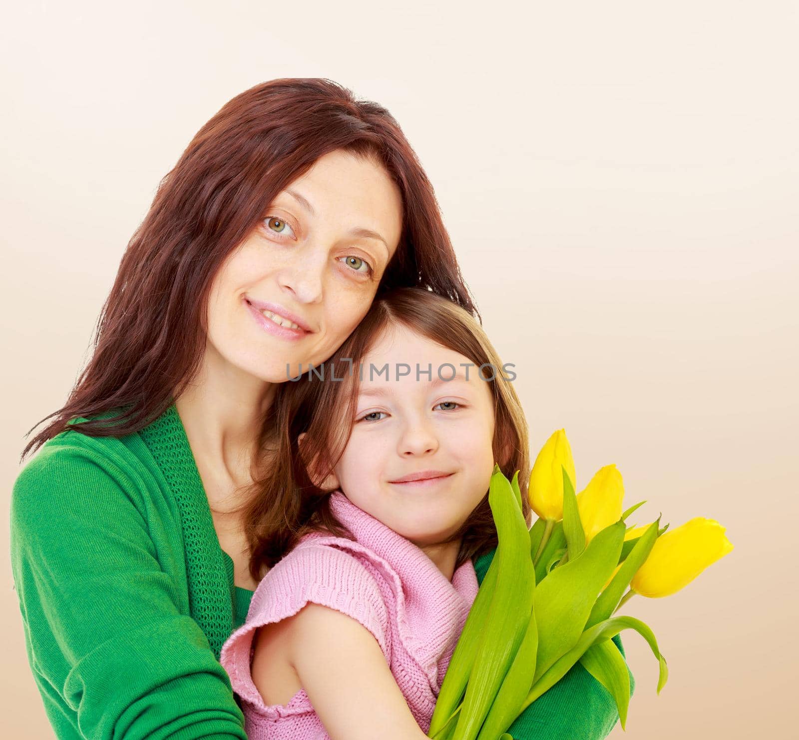 Happy mother gives her daughter a bouquet of yellow tulips.On a brown background.