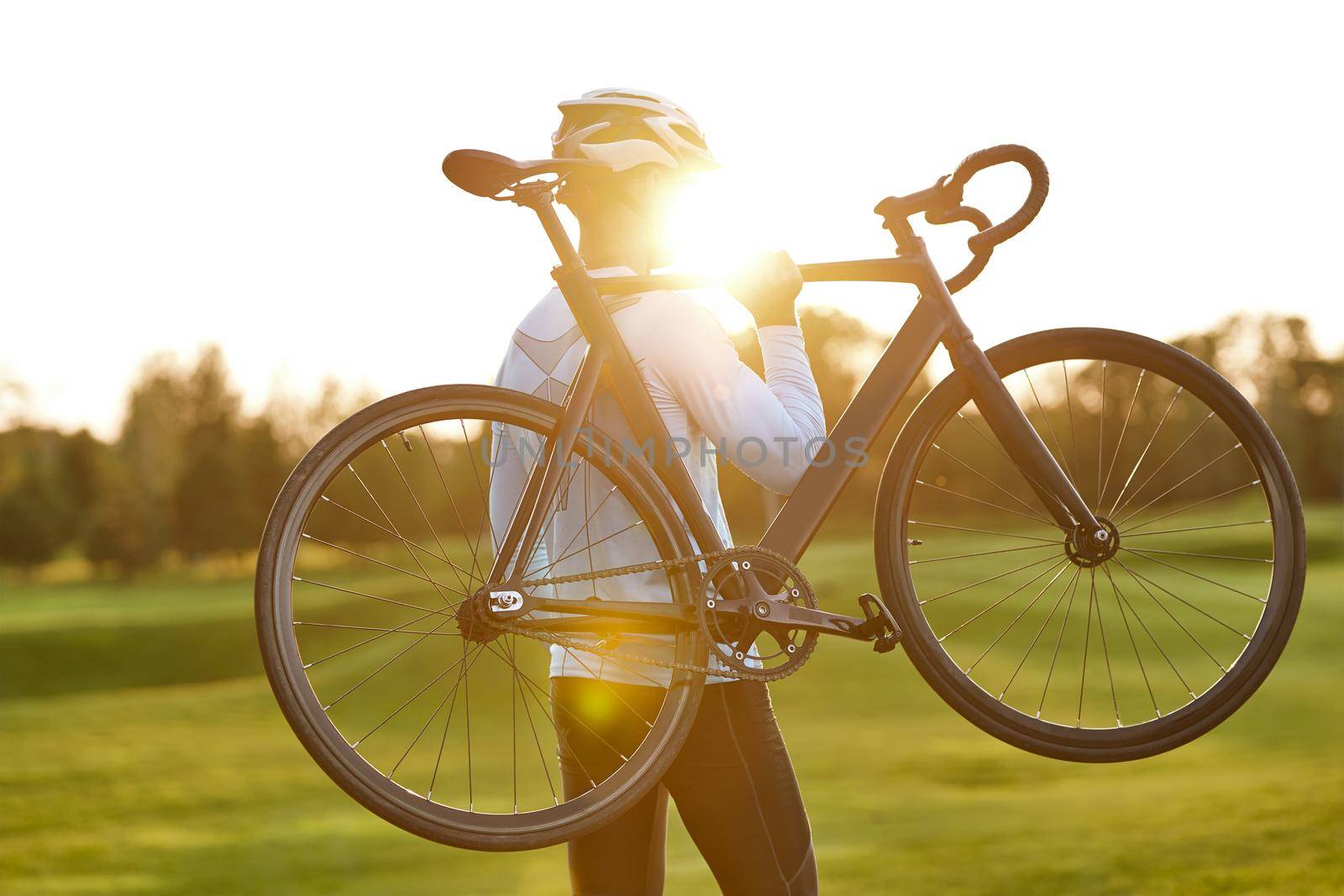 Strong athletic man in sportswear holding a bicycle while standing in park at sunset, cycling outdoors and enjoying amazing nature view. Active lifestyle and sport