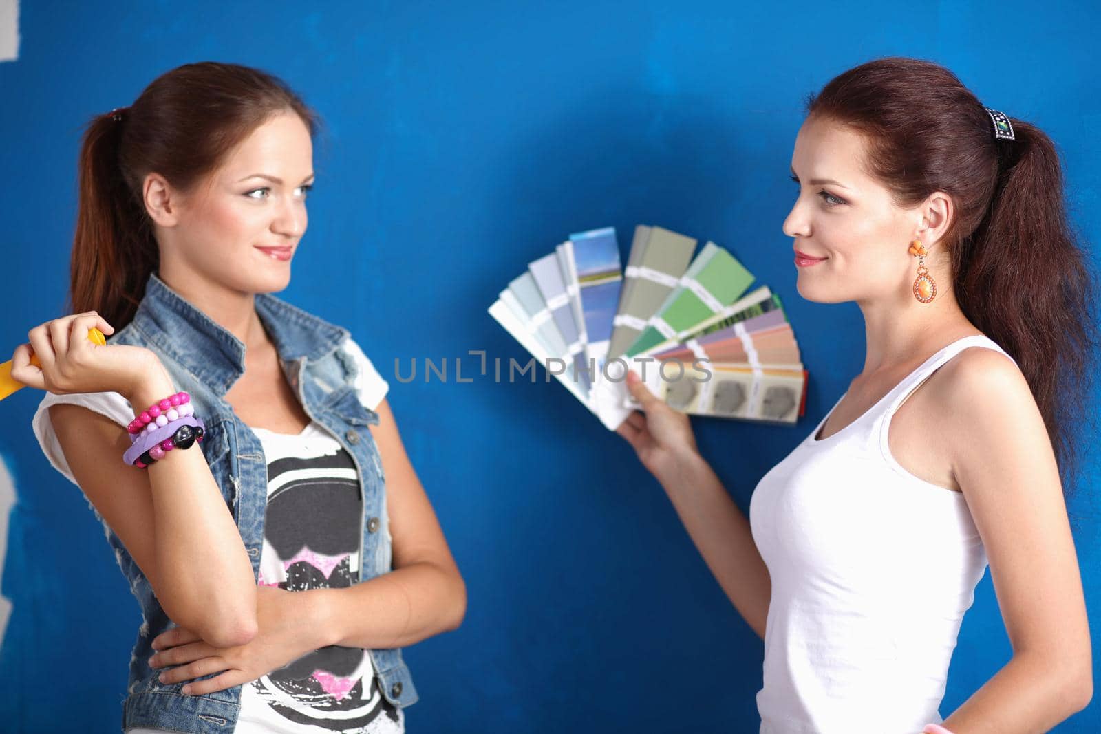 Two Young beautiful women holding color palette , standing near wall. by lenetstan