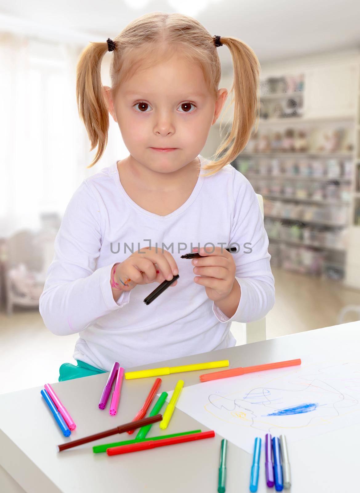 The concept of family happiness,and preschool education of the child , against a child's room with bookshelves.Pretty little blonde girl drawing with markers at the table.Girl holding in hands