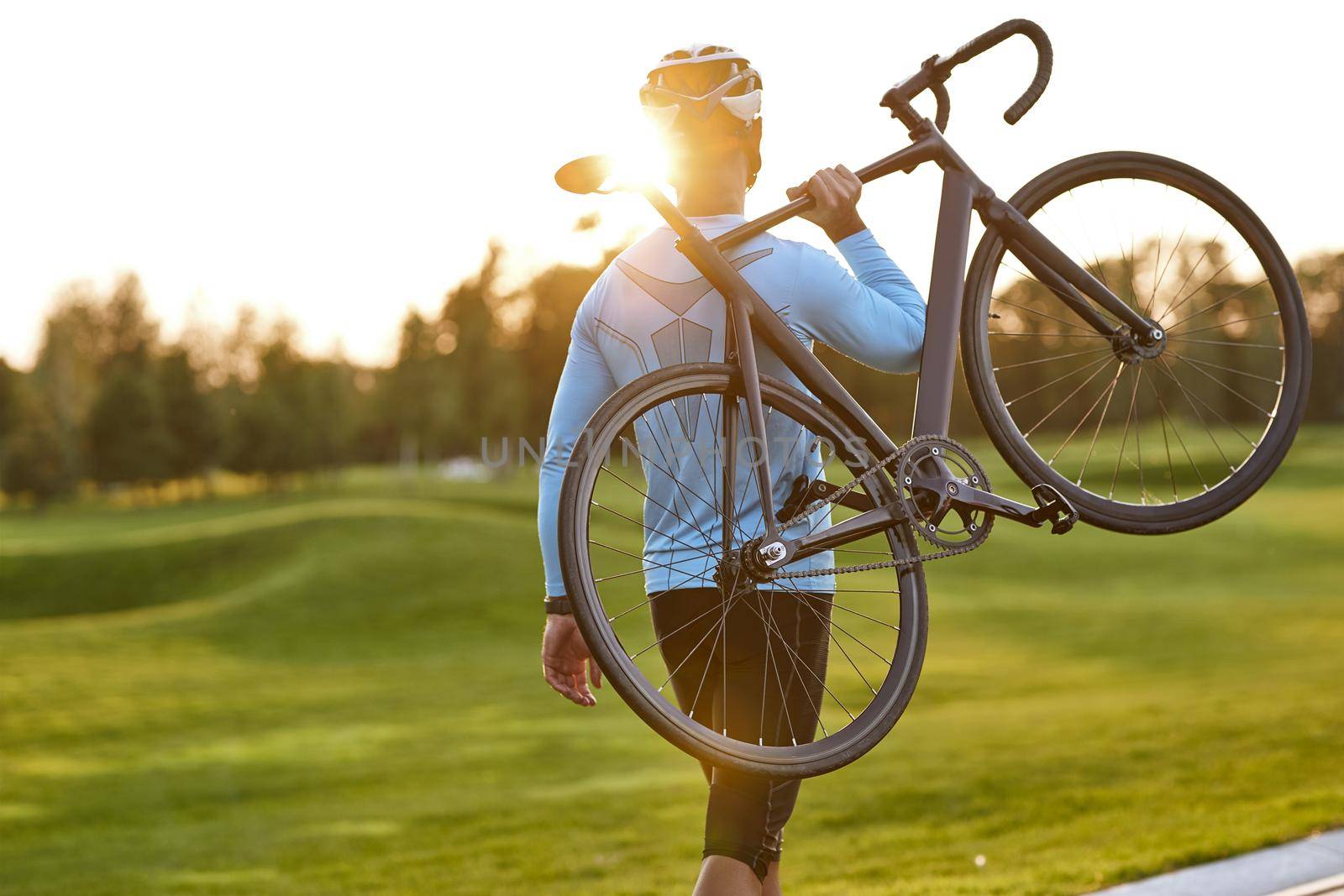 Strong athletic man in sportswear carrying his bicycle and watching amazing sunset after cycling in park by friendsstock