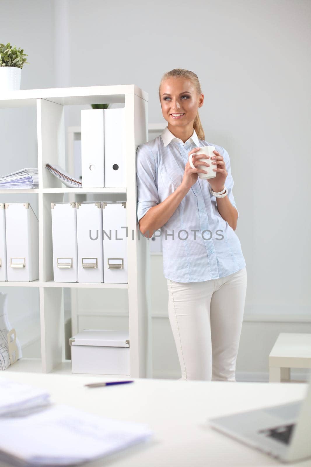 Attractive young businesswoman standing near desk in the office.