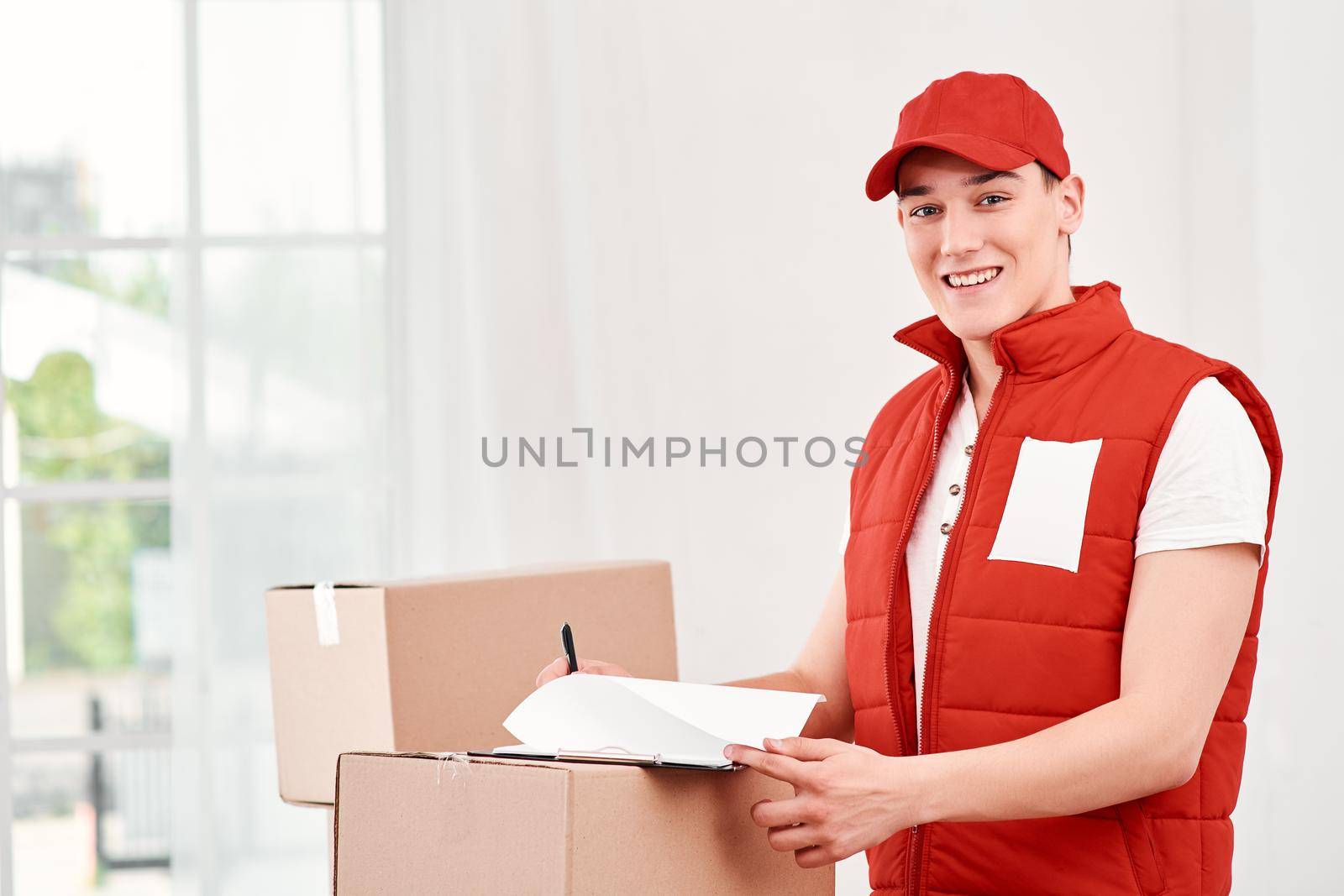 A lot to do. Smiling delivery man standing with packages and clipboard by friendsstock