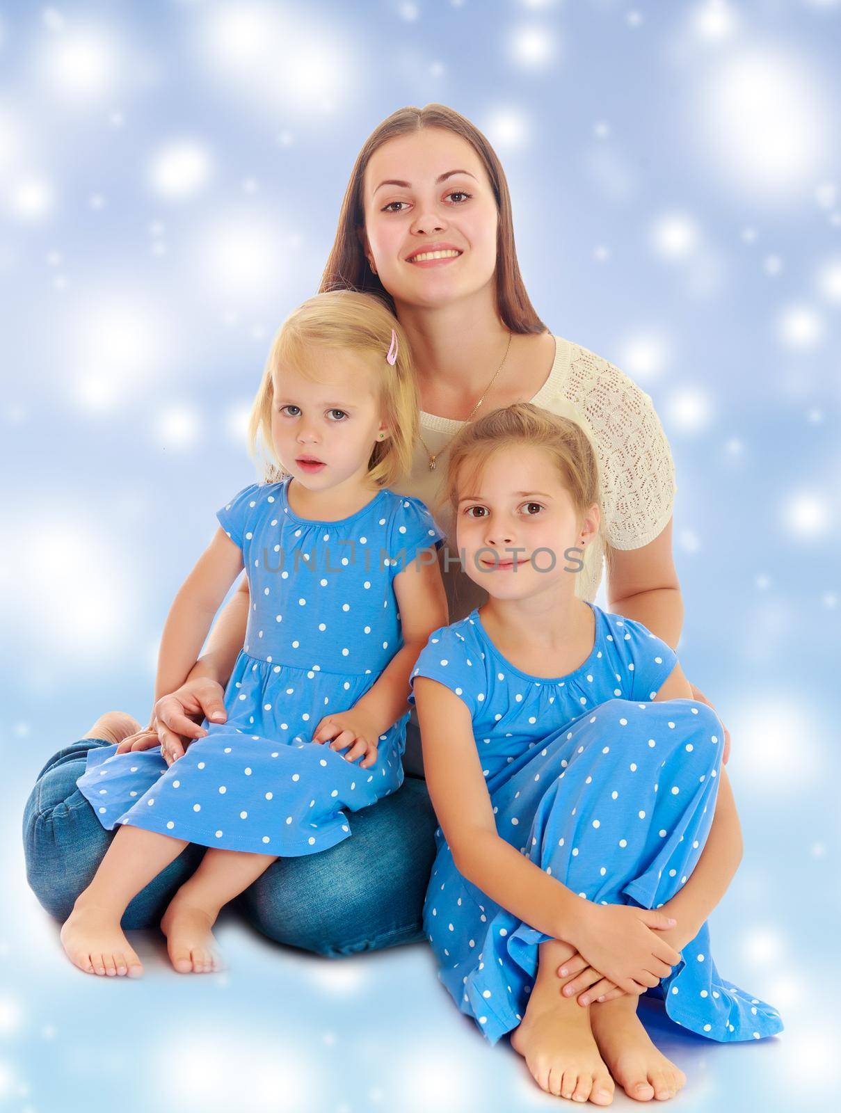 Beautiful young mother with her two daughters. Girls in the same dress with polka dots. Look directly at the camera.The concept of family happiness and mutual understanding between parents
