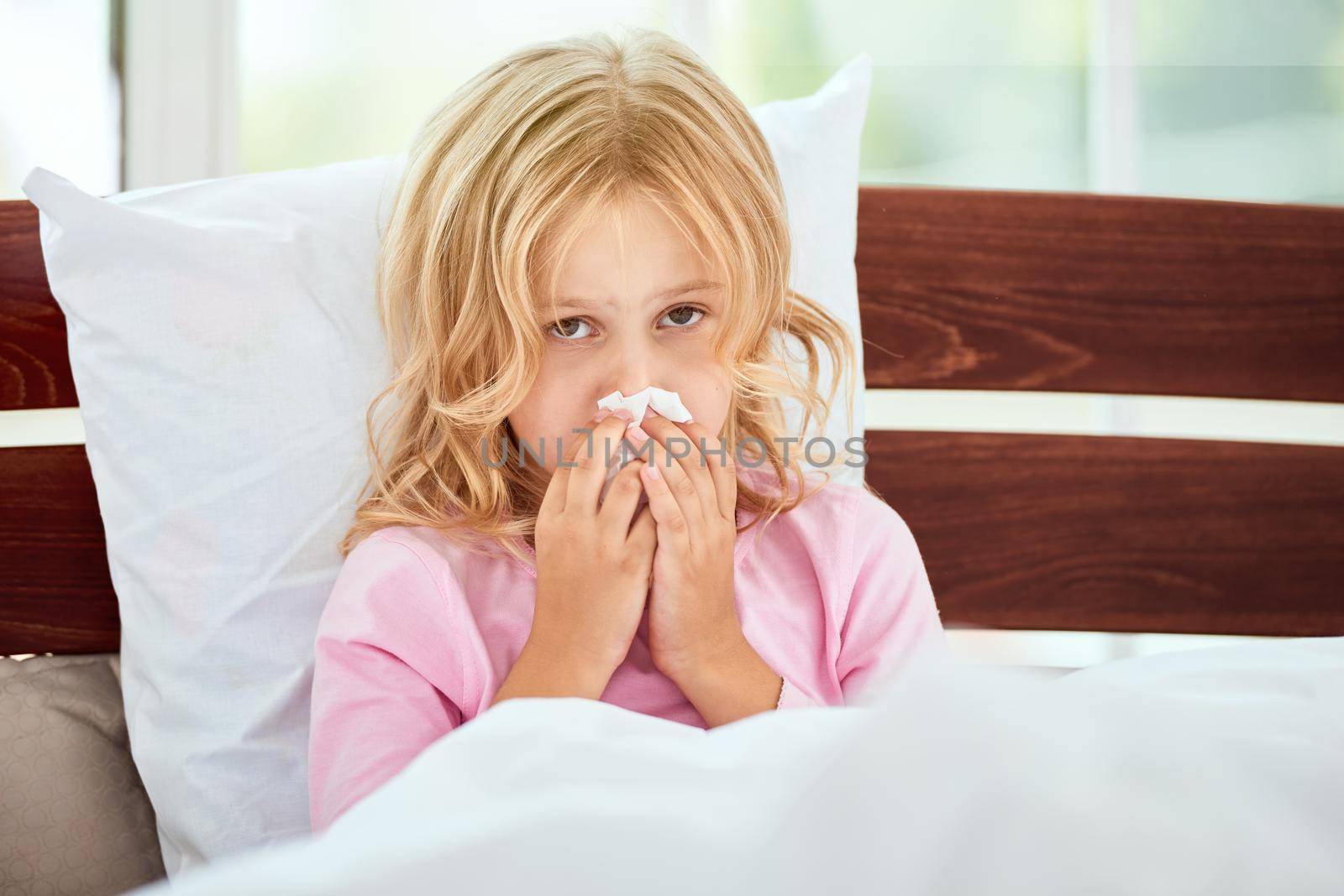 Portrait of little girl with runny nose suffering from cold or flu while lying in bed at home. Virus disease. Coronavirus concept. Healthcare concept