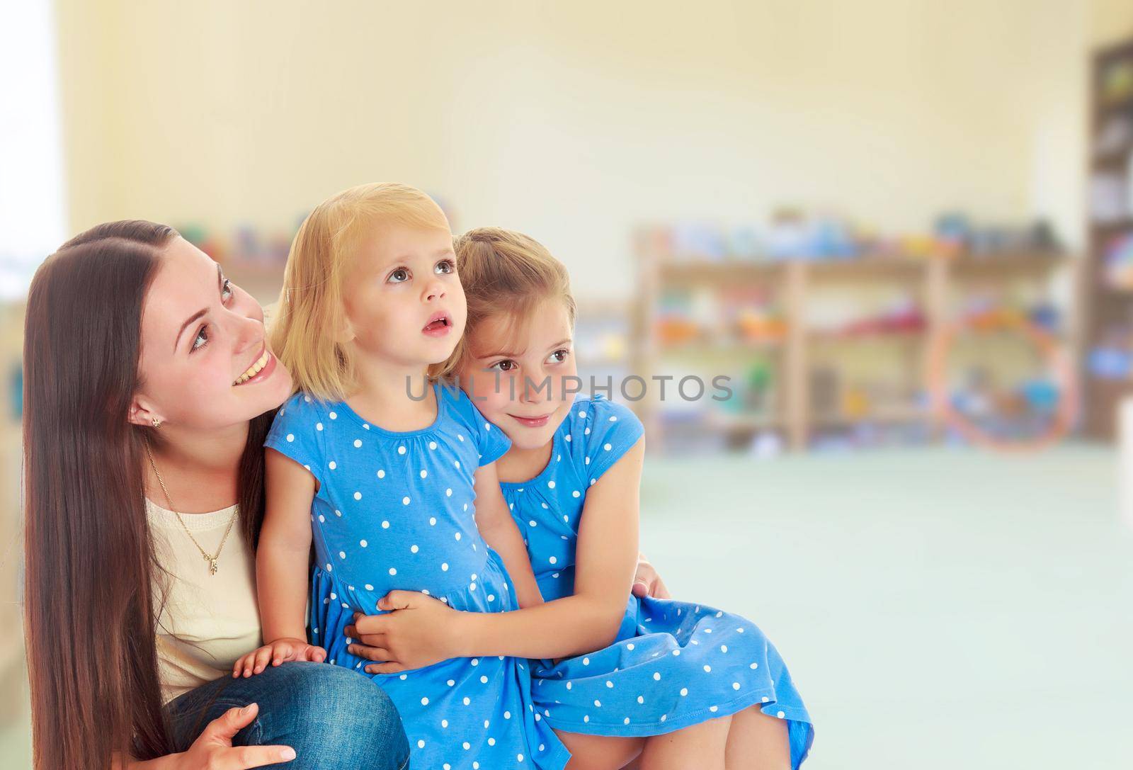 Beautiful young mother with her two daughters. All look up.The concept of family happiness and mutual understanding between parents and children.On the background of the room where children