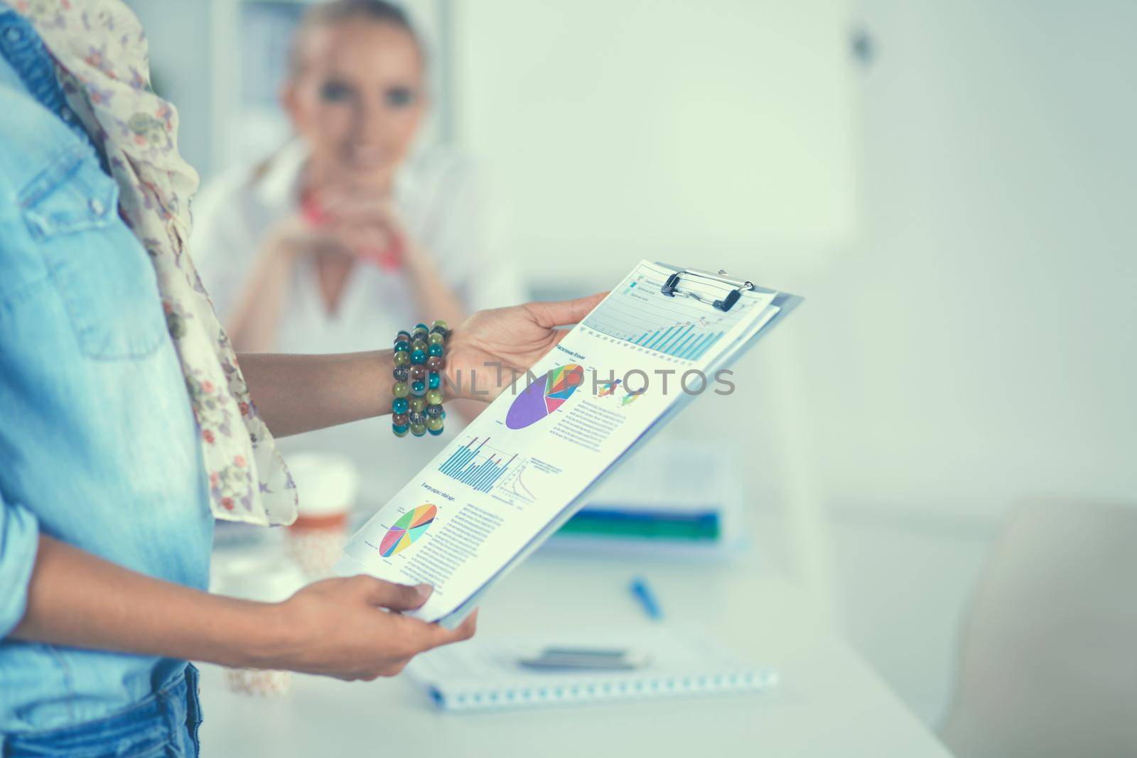 Two women working together at office, sitting on the desk.