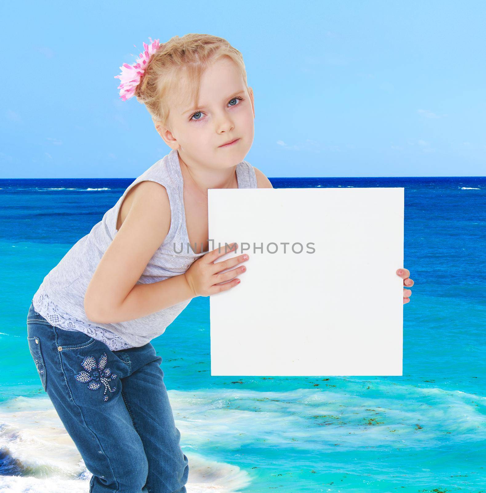 Girl in gray shirt holding a white banner on the background of the sea.