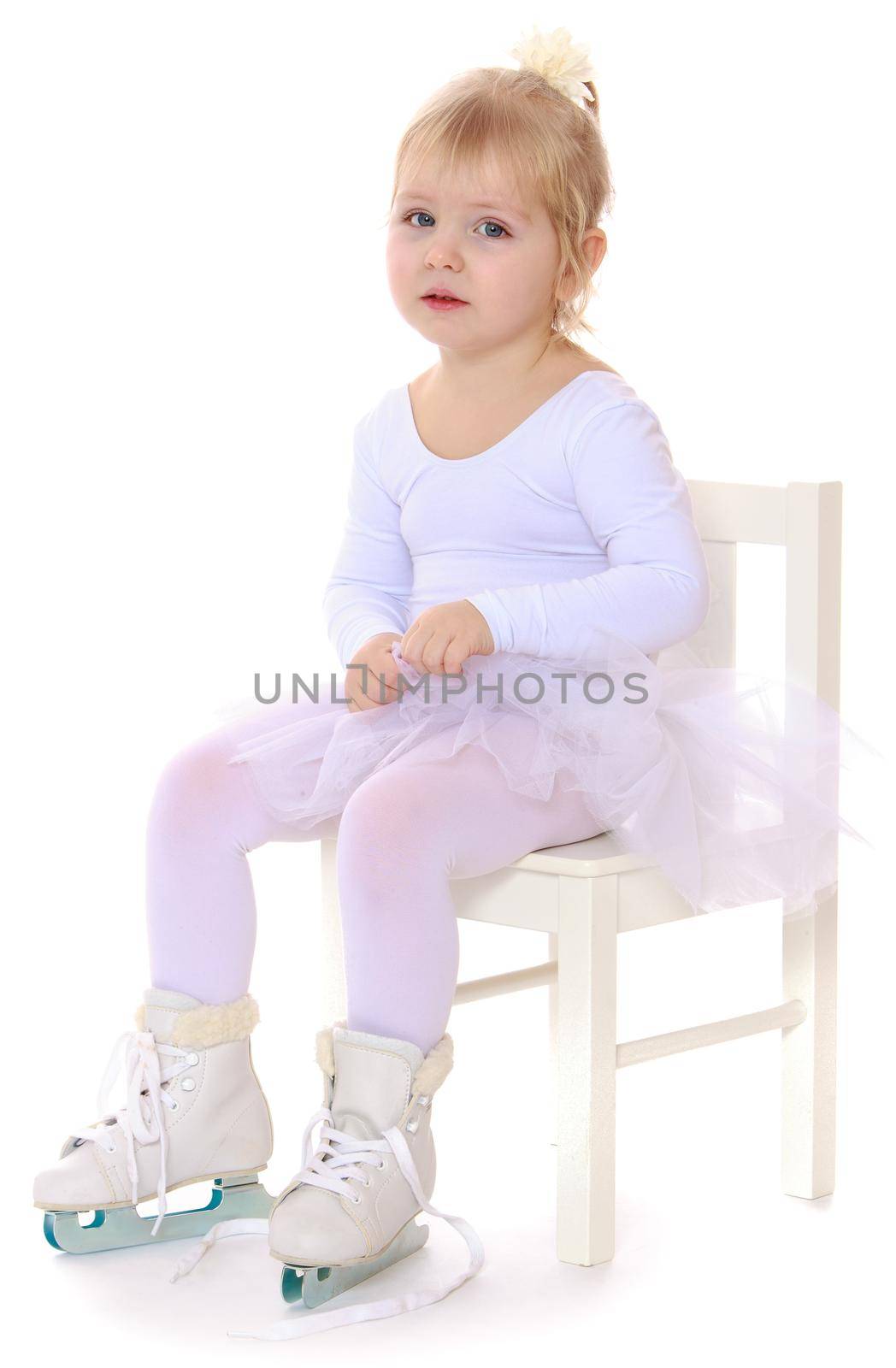 Cute little girl , a future figure skater, sits on a chair in a White sports dress and figure skates on two skids-Isolated on white background