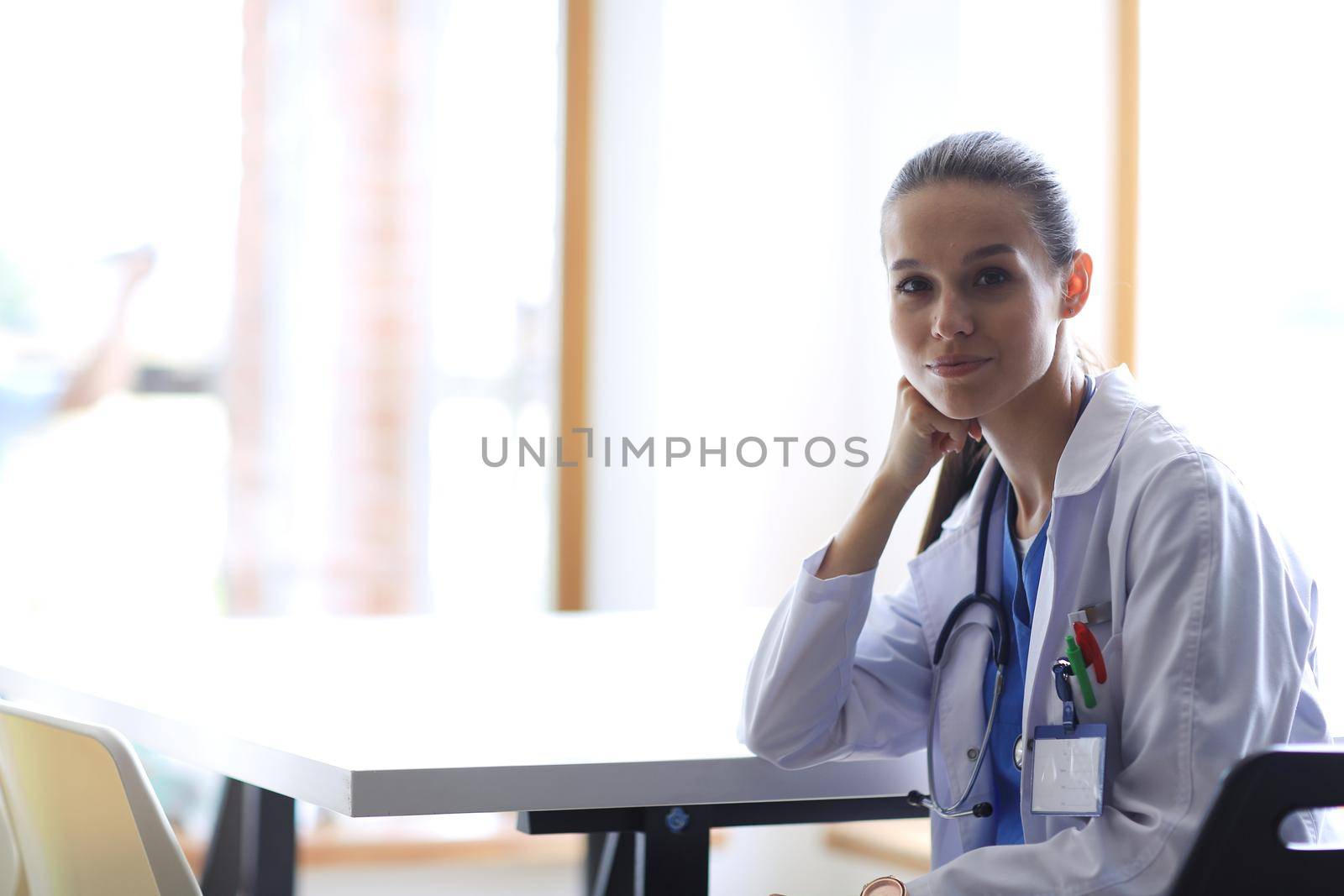 Beautiful young smiling female doctor sitting at the desk. Woman doctor by lenetstan