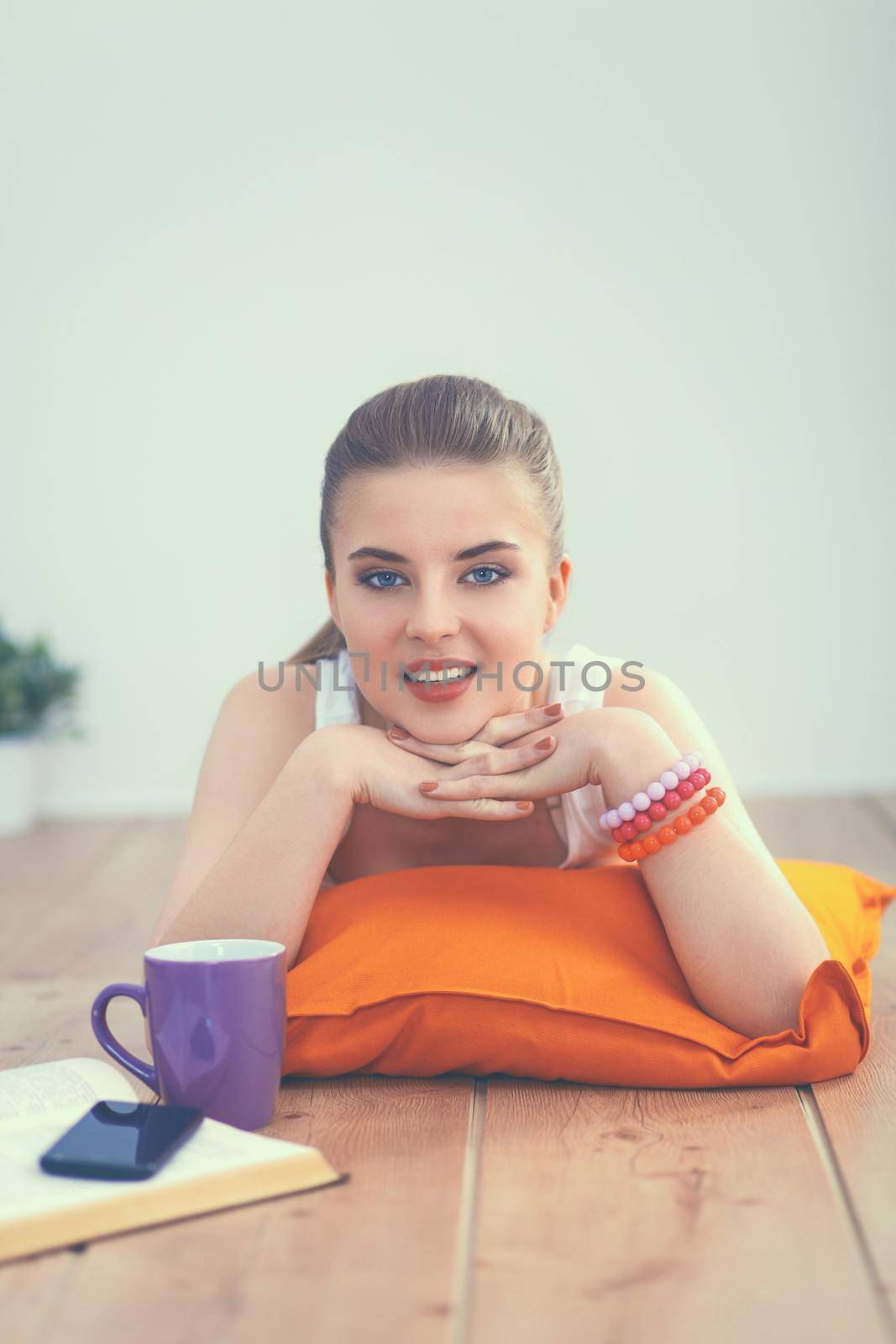 Smiling young woman lying on a white floor with pillow.