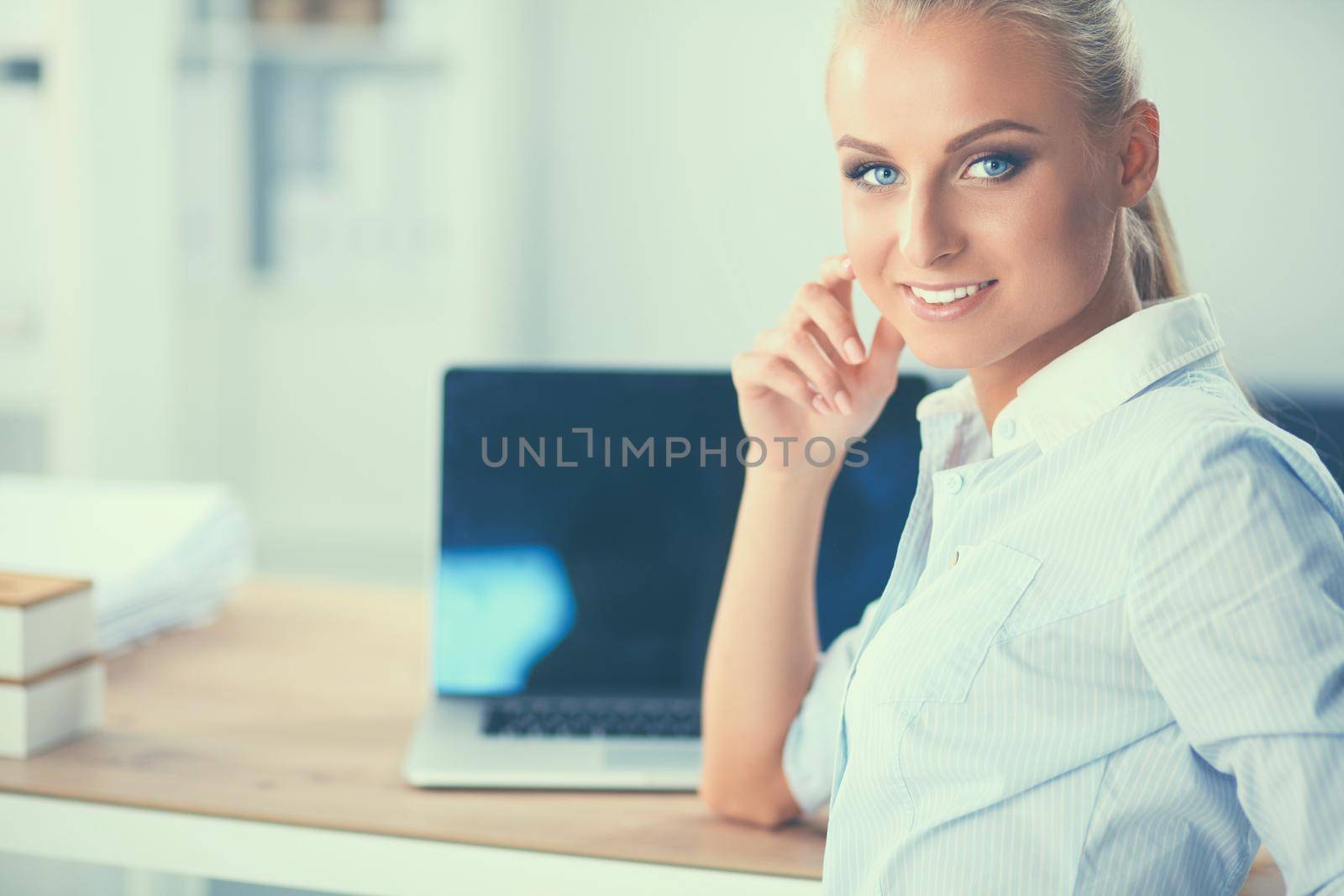 Attractive businesswoman sitting on a desk with laptop in the office.