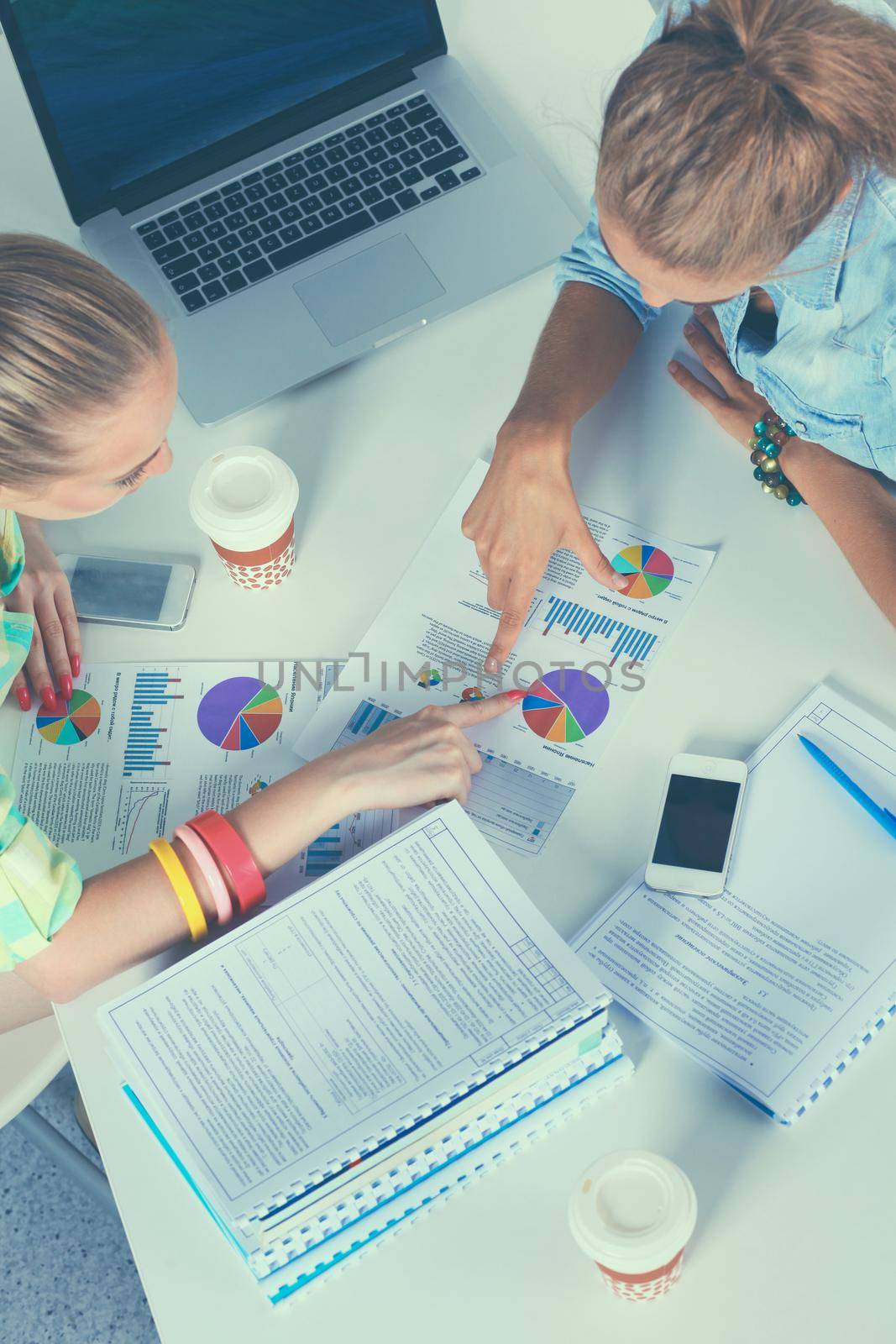 Two women working together at office, sitting on the desk.