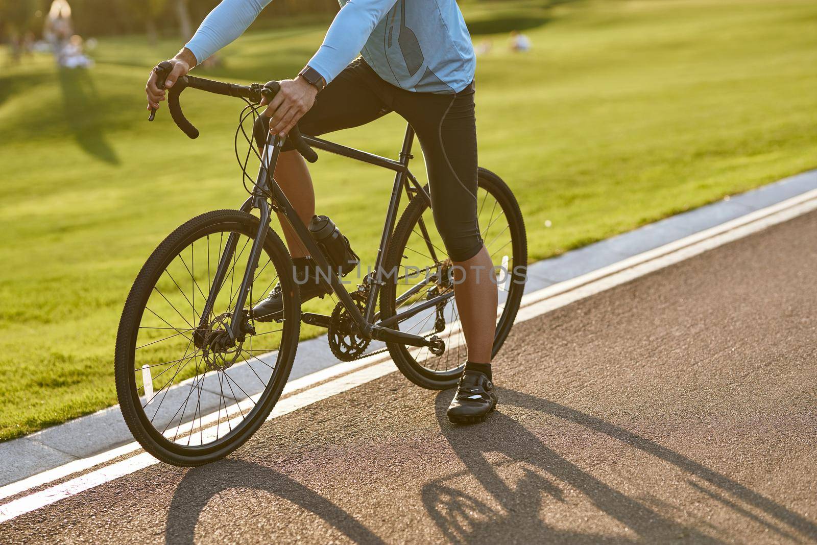 Cycling at sunset. Cropped shot of a man in sportswear standing with his bicycle on the road in park on a summer day. Active lifestyle and sport