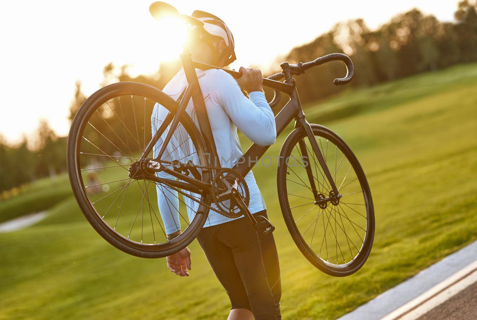 Strong athletic man in sportswear and protective helmet carrying his bicycle after cycling training in park, enjoying amazing sunset. Active lifestyle and sport concept. Biking outdoors