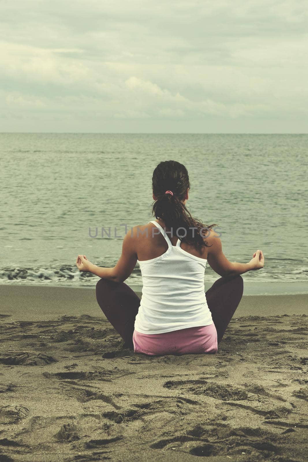 young woman meditating yoga in lotus positin on the beach at early morning