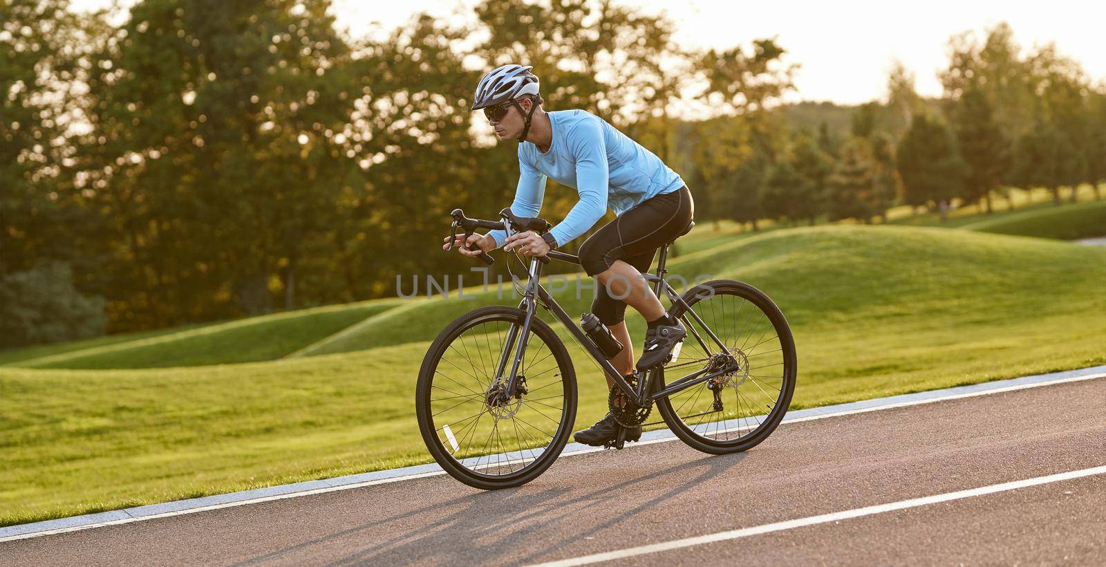Professional bicycle racer in action. Side view of a young athletic man in sportswear riding mountain road bike at sunset. Healthy active lifestyle and sport concept