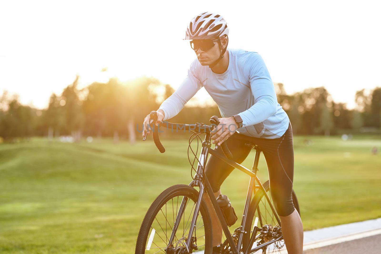 Professional road bicycle racer in sportswear and protective helmet standing on the road at sunset, ready to ride. Man cycling in the park by friendsstock