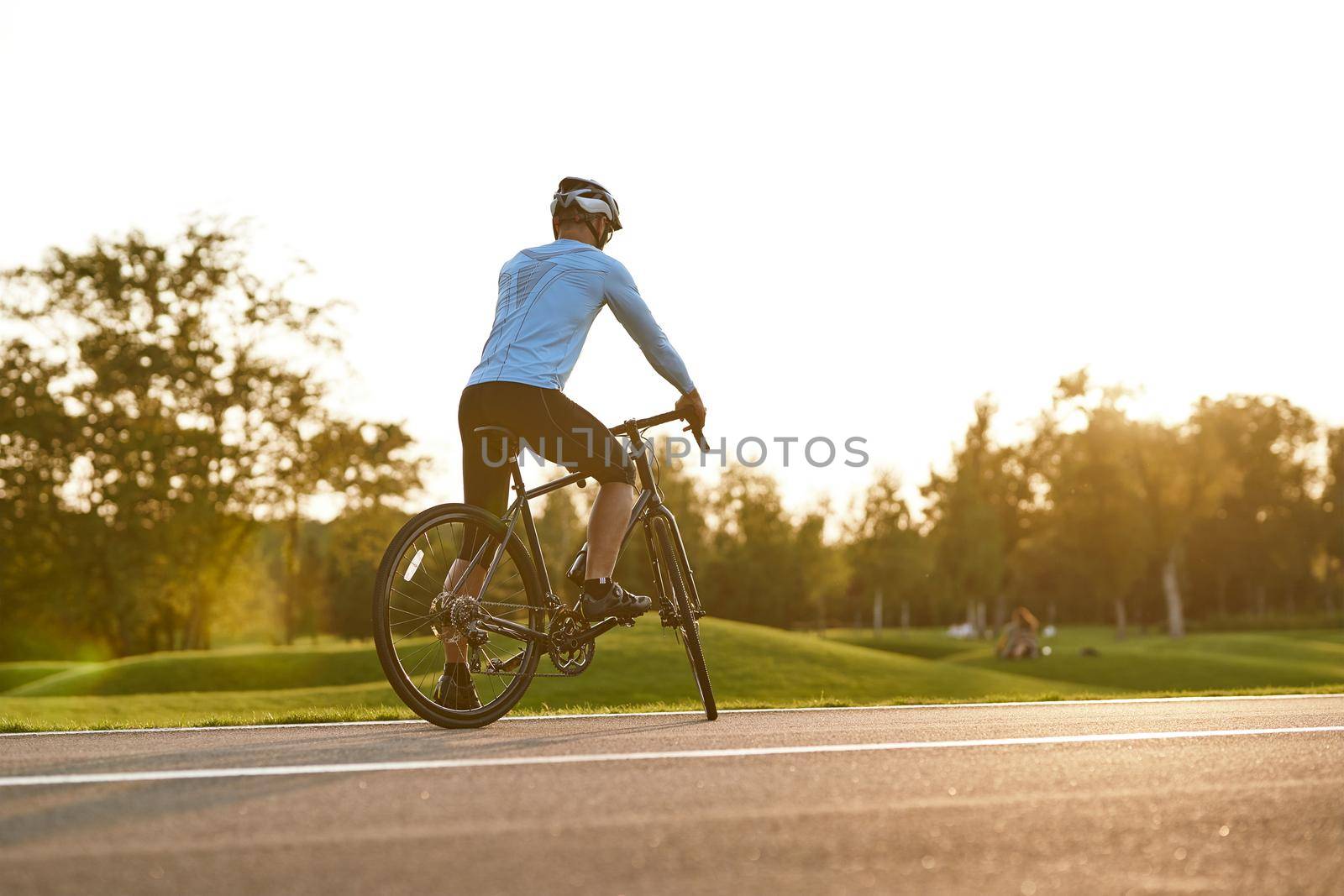 Ready to ride. Rear view of athletic man in sportswear cycling outdoors at sunset, professional racer standing with bicycle on the road and enjoying amazing nature view. Active lifestyle and sport