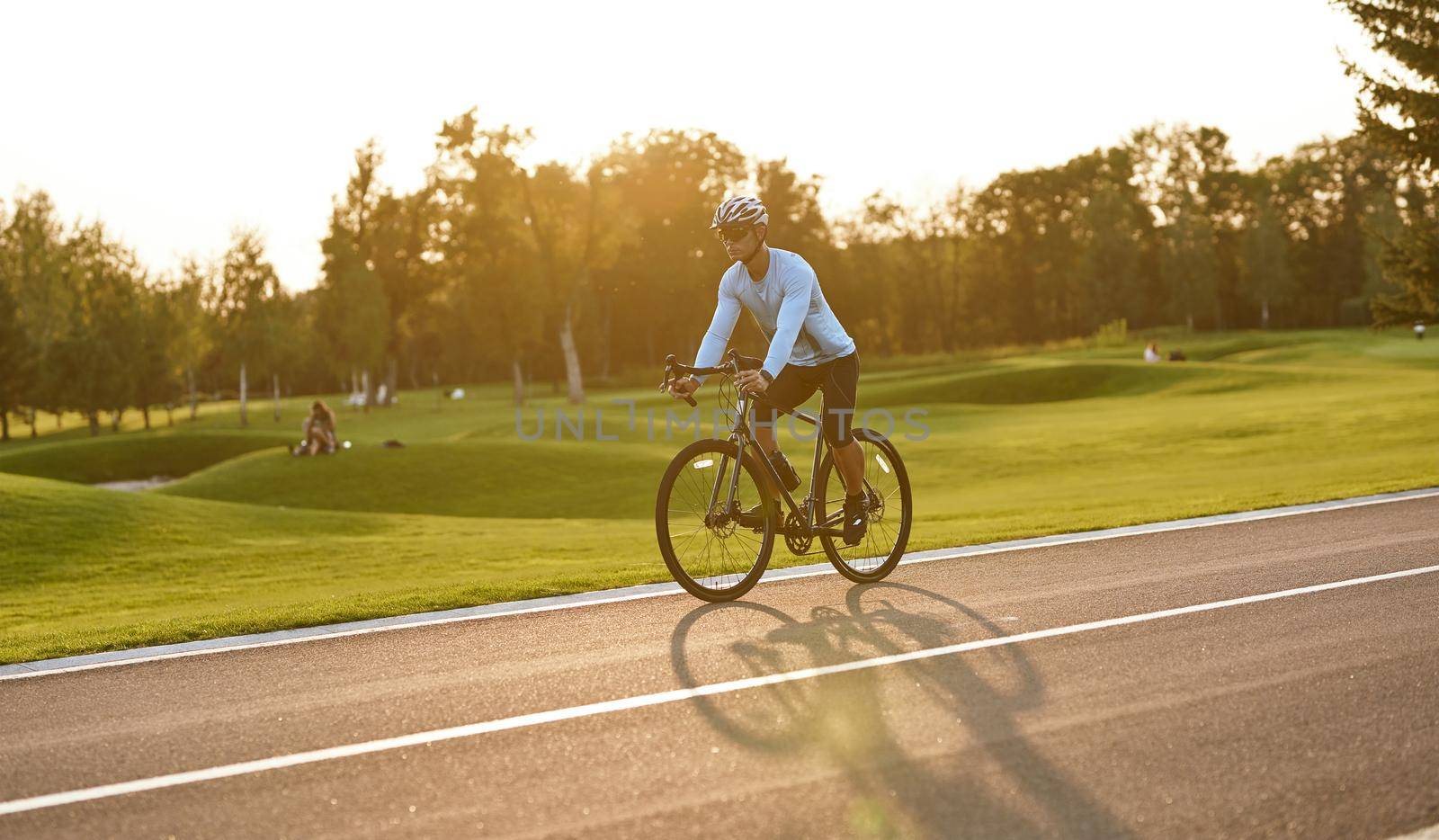 Side view of a young athletic man in sportswear cycling in city park at sunset, riding mountain road bike by friendsstock