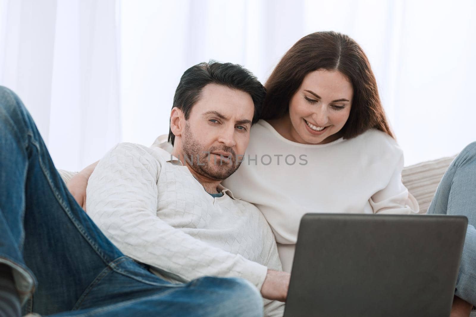 happy couple sitting on the couch in her arms, looking at laptop by asdf