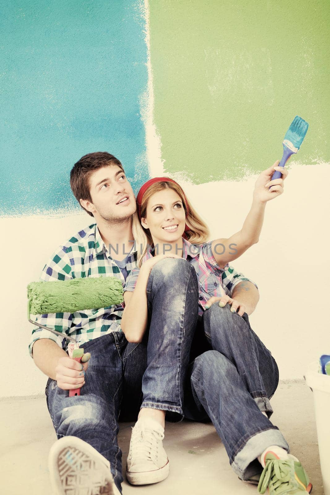 happy young couple paint in green and blue color white wall of their new home