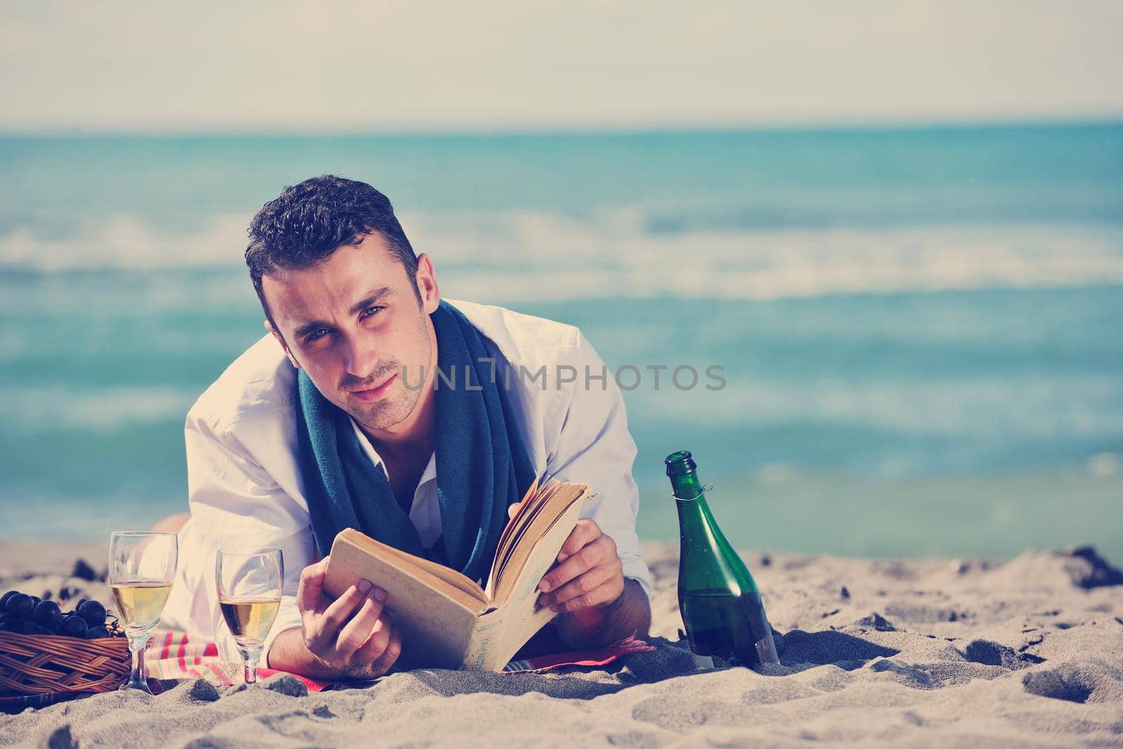 young man relaxing on beach at beautiful sunny day while reading book representing summer school and education concept