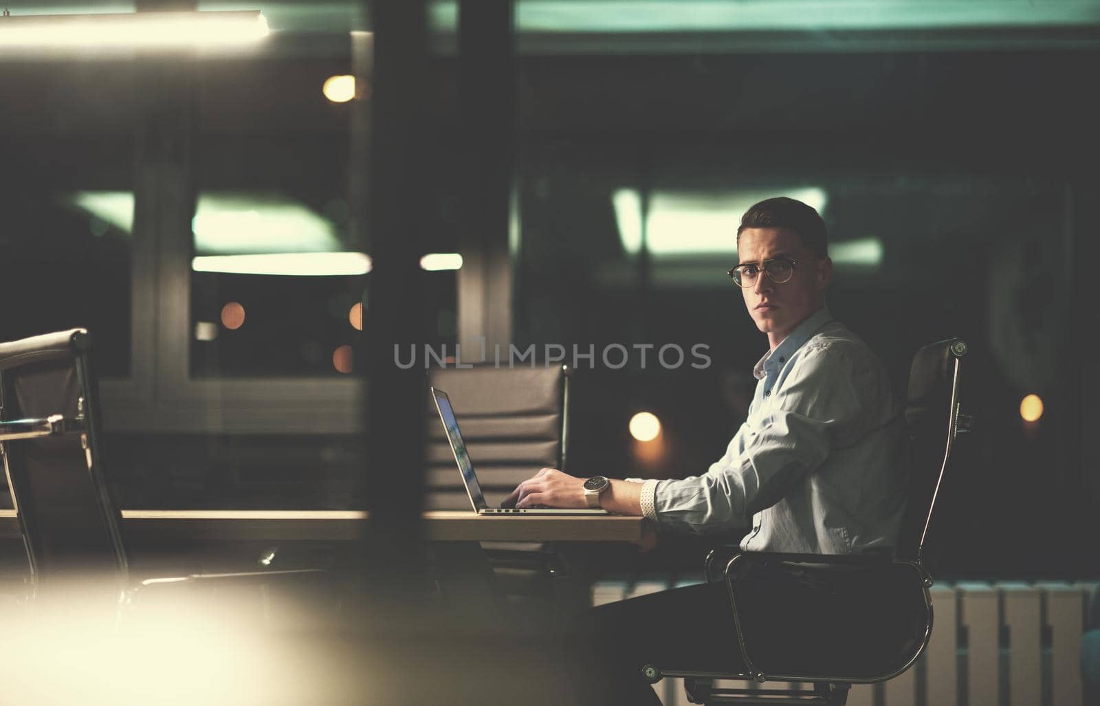 Young man working on laptop at night in dark office. The designer works in the later time.