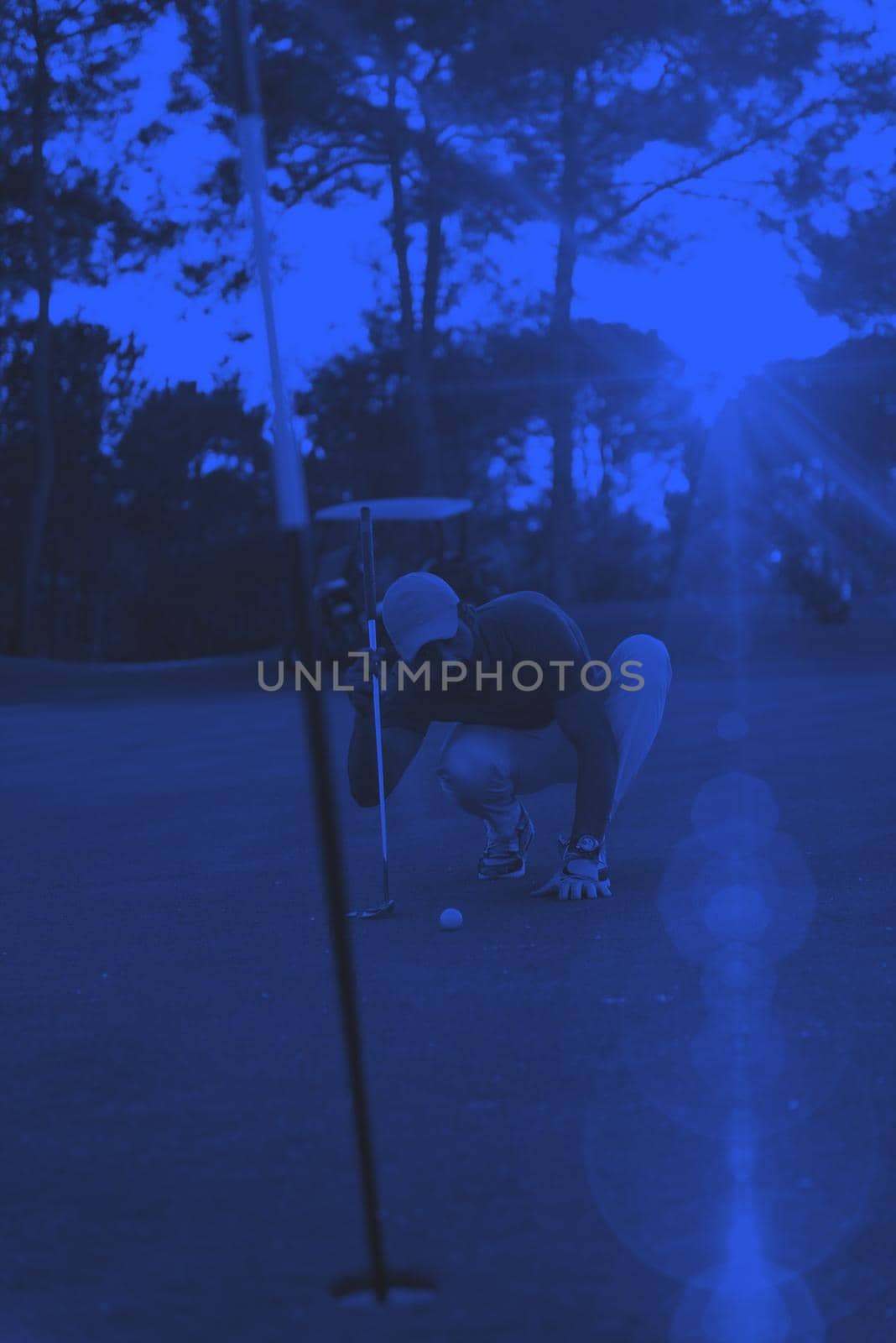 golf player aiming shot with club on course at beautiful sunset with sun flare in background duo tone