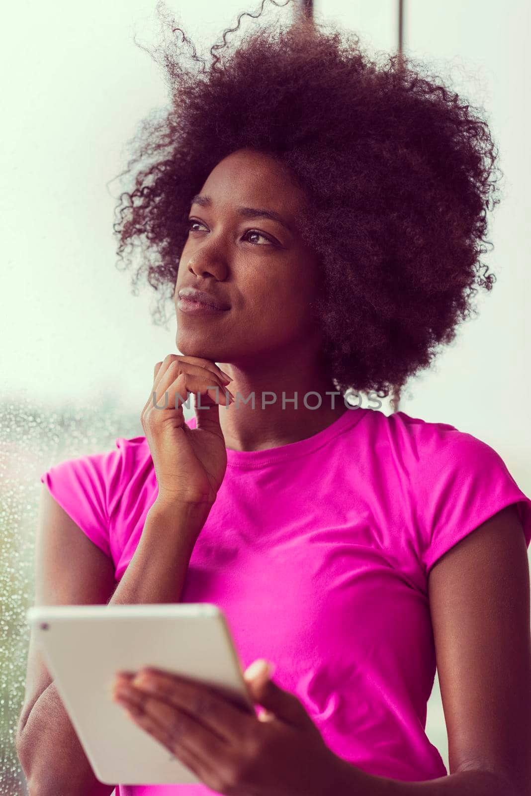 beautiful african american woman using tablet computer from home while rain and bad weather is outdoor