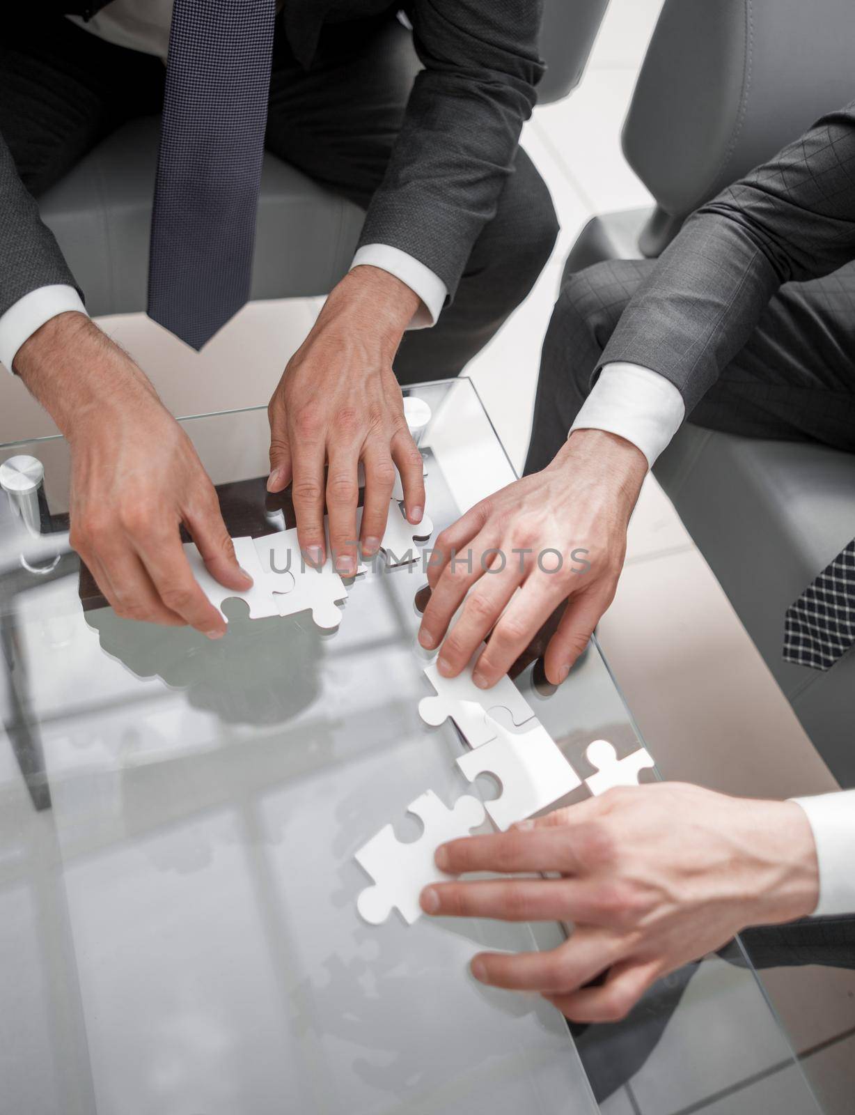 close up.business people putting together a puzzle ,sitting behind a Desk by asdf