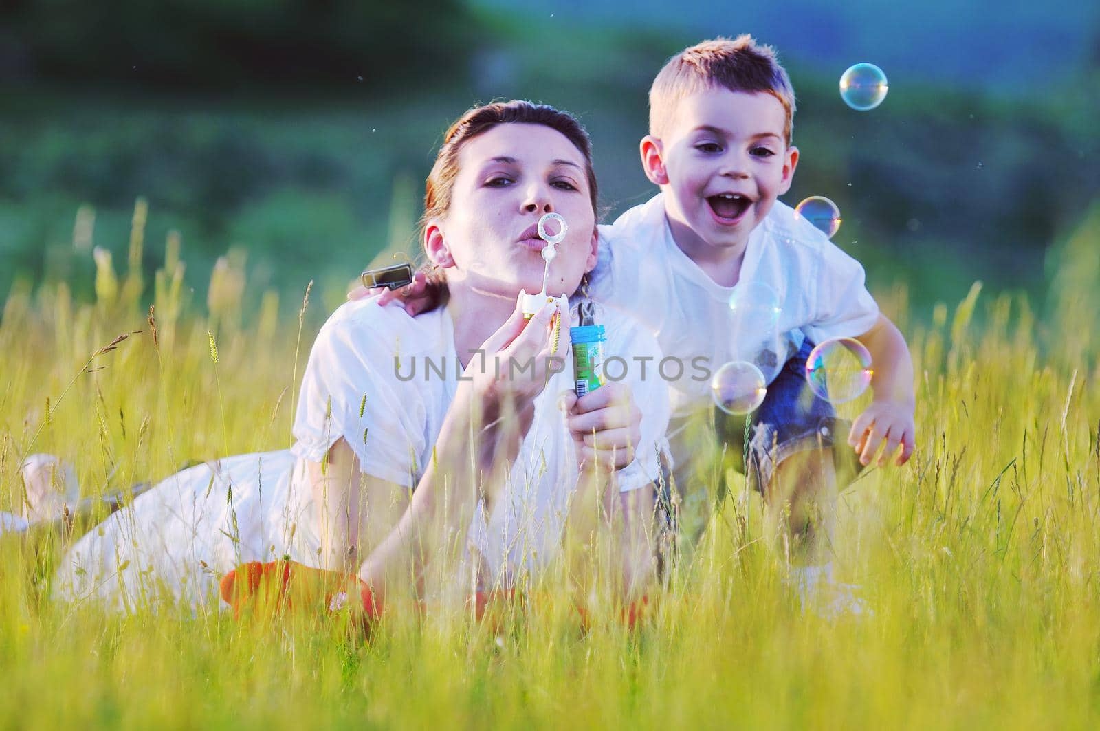 happy child and woman outdoor playing with soap bubble on meadow