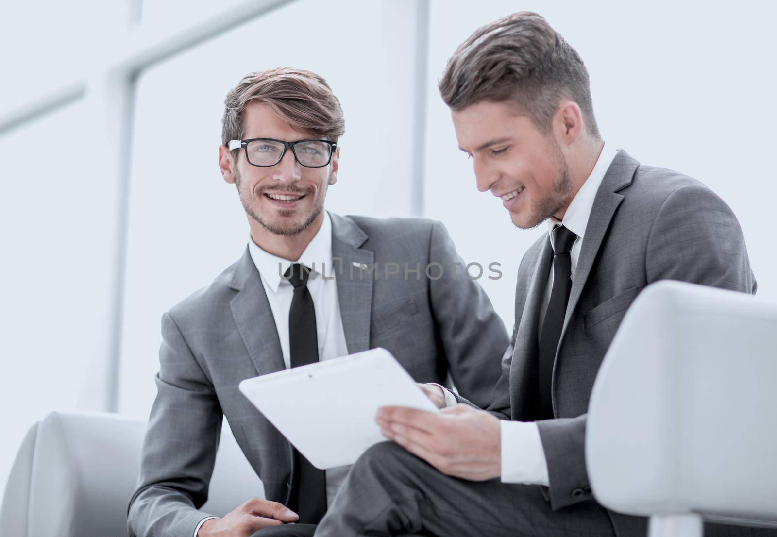 Smiling young businessman discussing something positive with his colleague, and using a digital tablet together