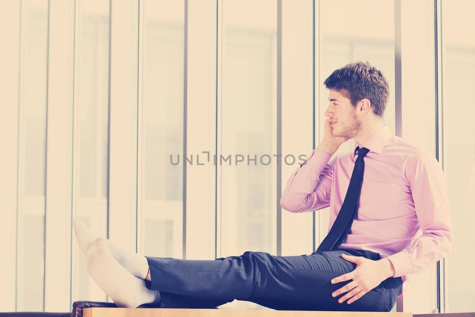 young business man talk by cellphone over bright window in big hall