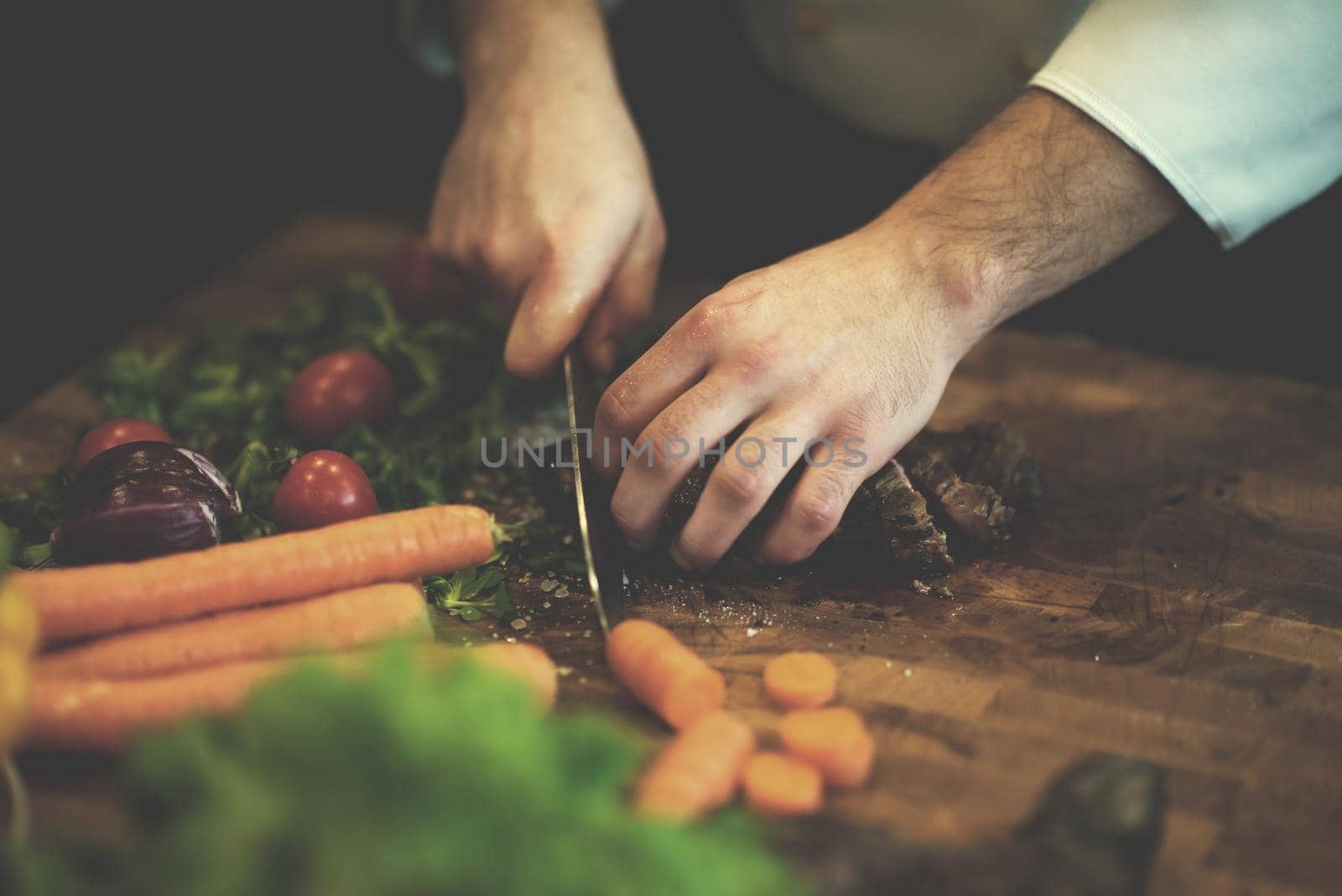 closeup of Chef hands in hotel or restaurant kitchen preparing beef steak with vegetable decoration