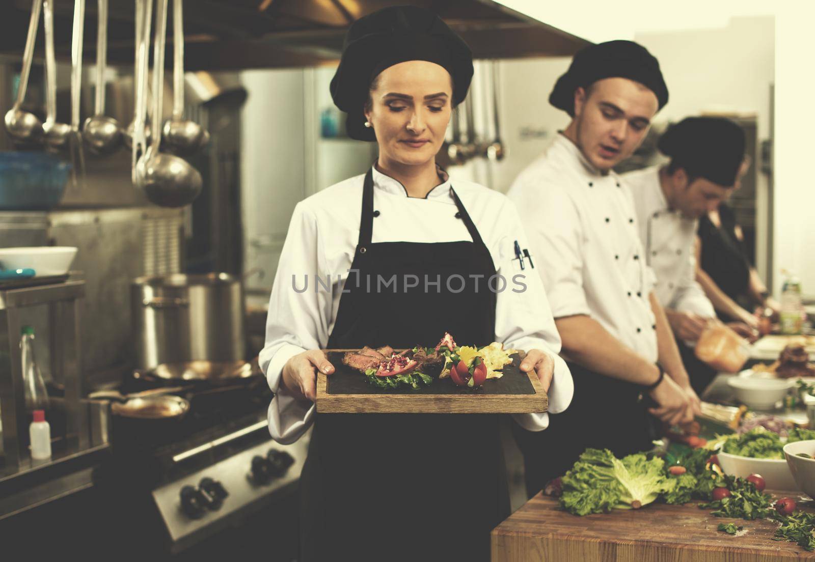 female Chef  in hotel or restaurant kitchen holding grilled beef steak plate with vegetable decoration