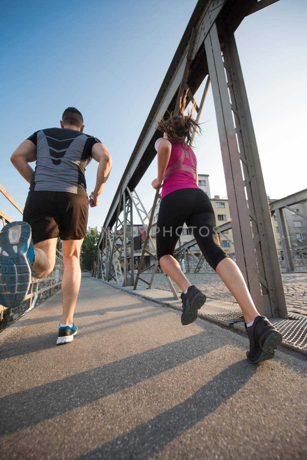 urban sports, healthy young couple jogging across the bridge in the city at sunny morning