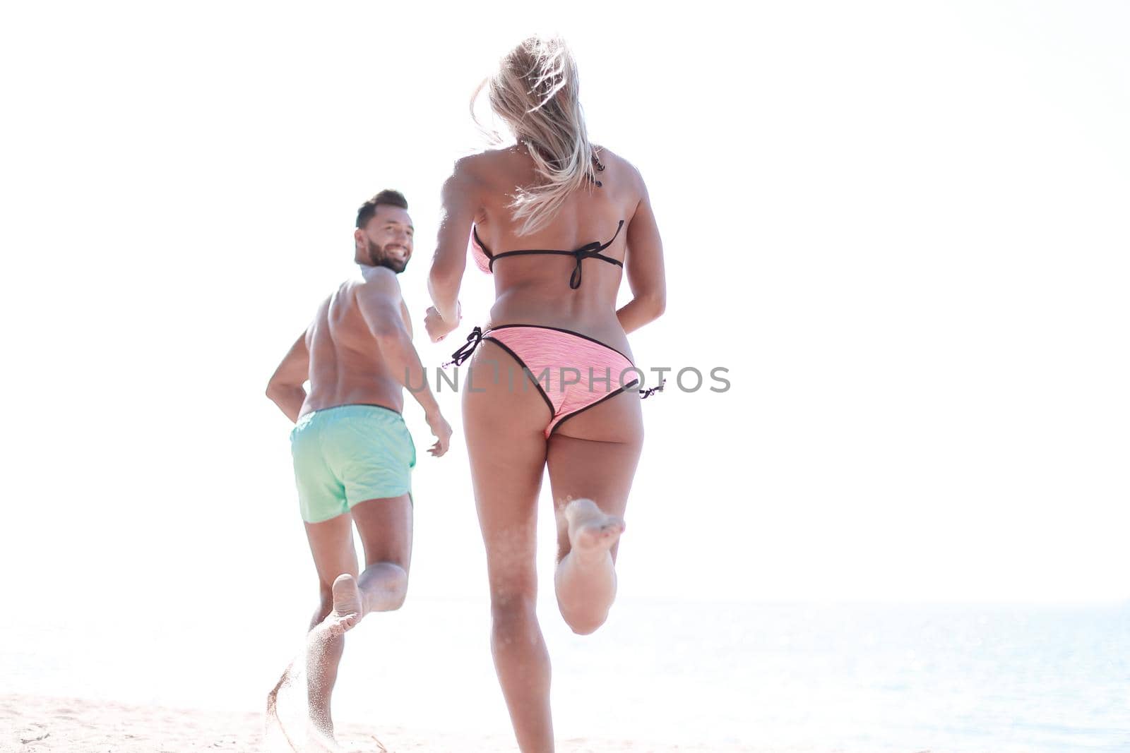 Happy couple running together among a beach at sunny day