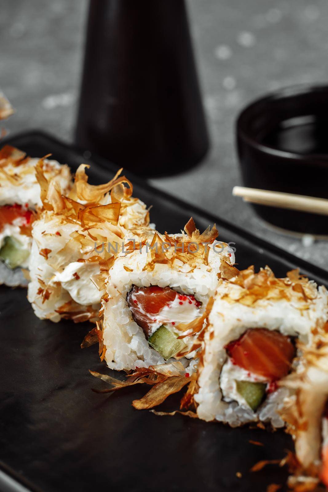 sushi rolls with cream cheese, fried salmon, tuna shavings or dried bonito, cucumber, nori. Chopsticks holding fresh katsuobushi roll in Japanese restaurant closeup by UcheaD