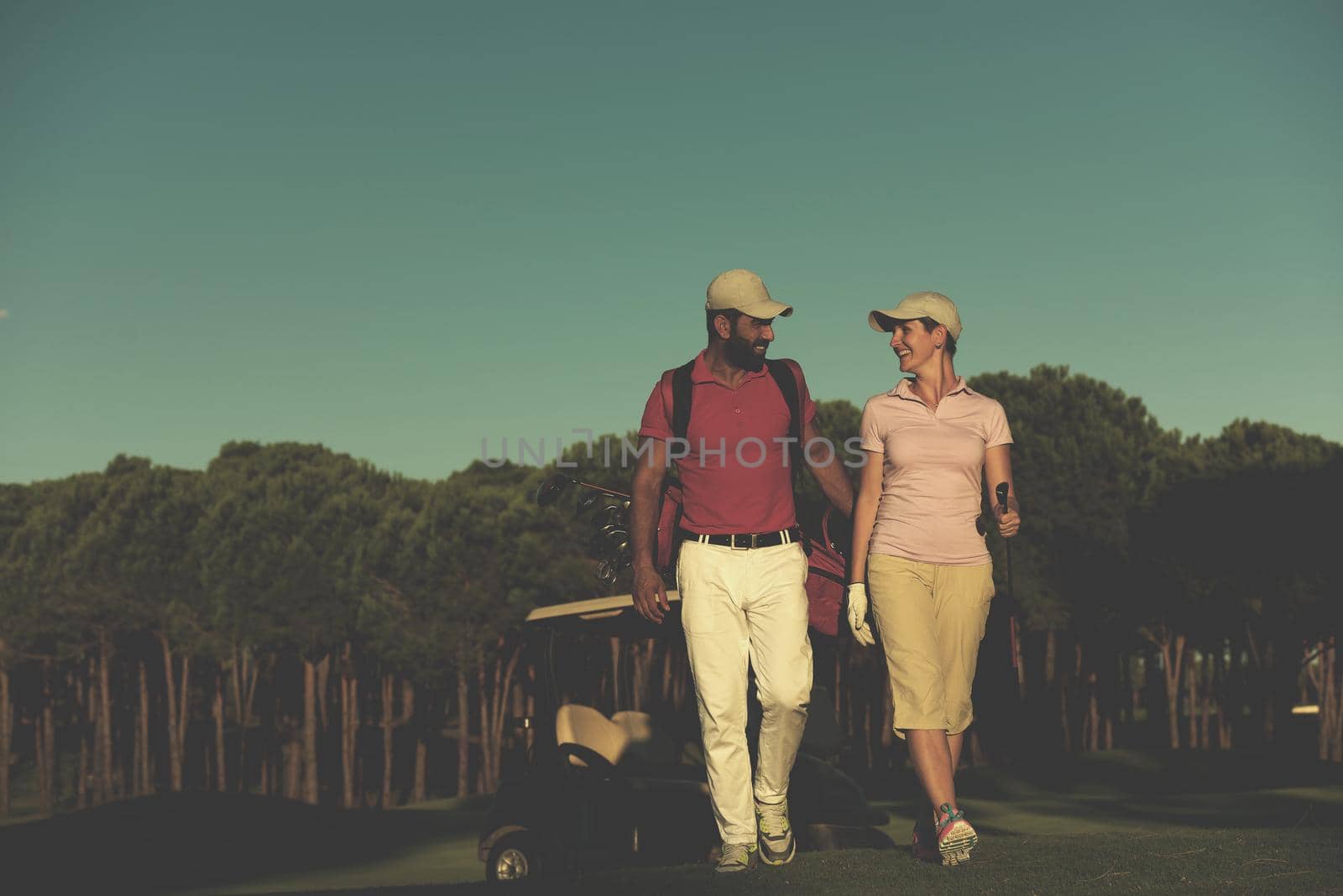 young couple walking to next hole on golf course. man carrying golf bag