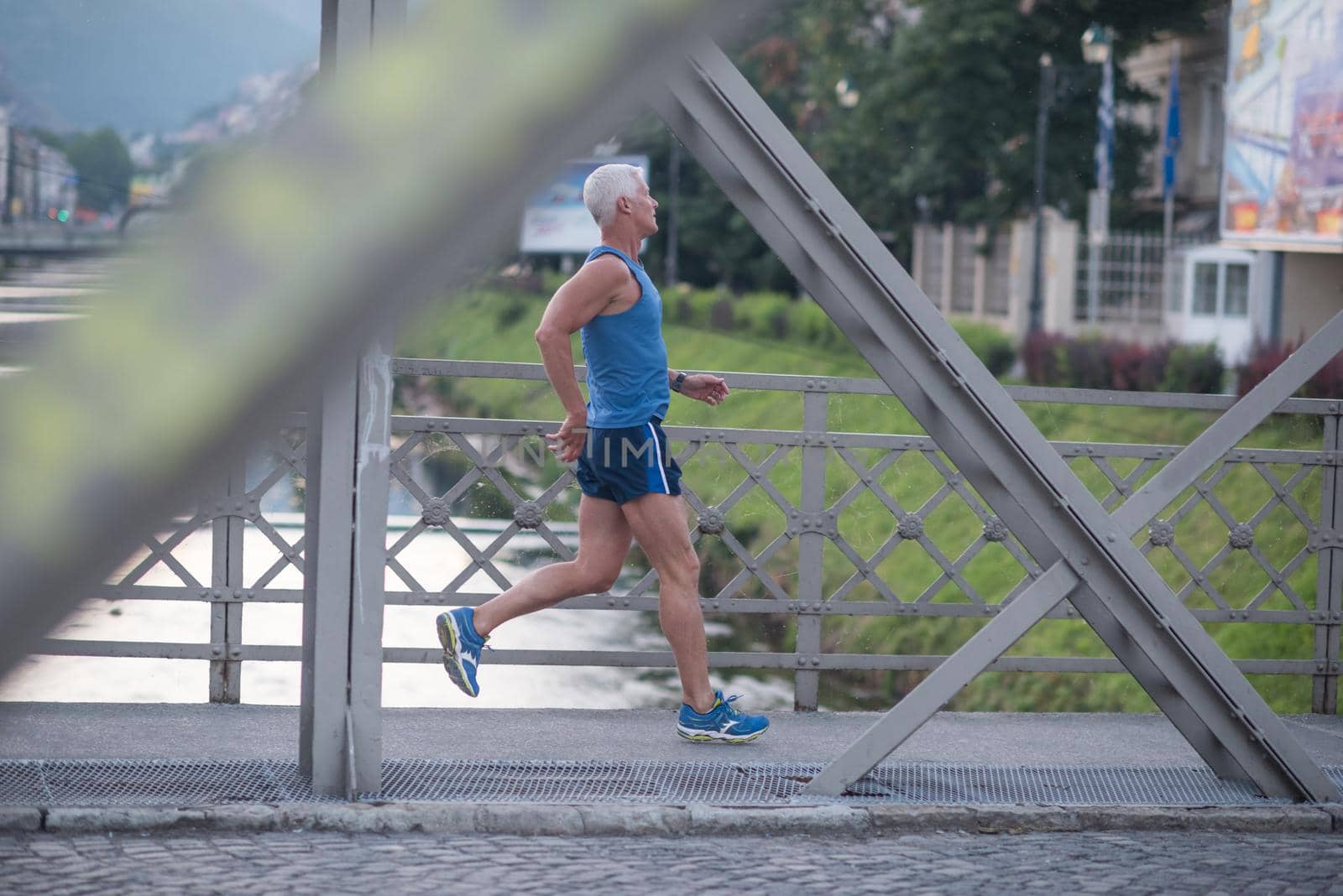 handsome senior man athlete jogging and  have morning workout with sunrise and city in background