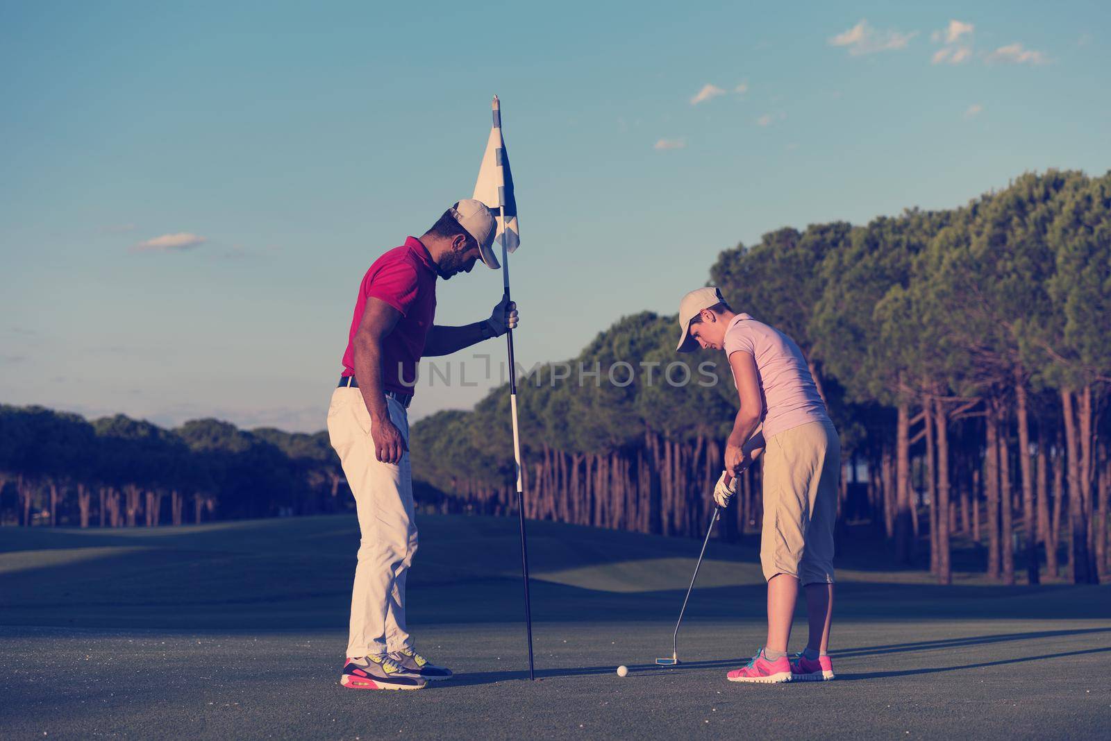 male golf instructor teaching female golf player, personal trainer giving lesson on golf course